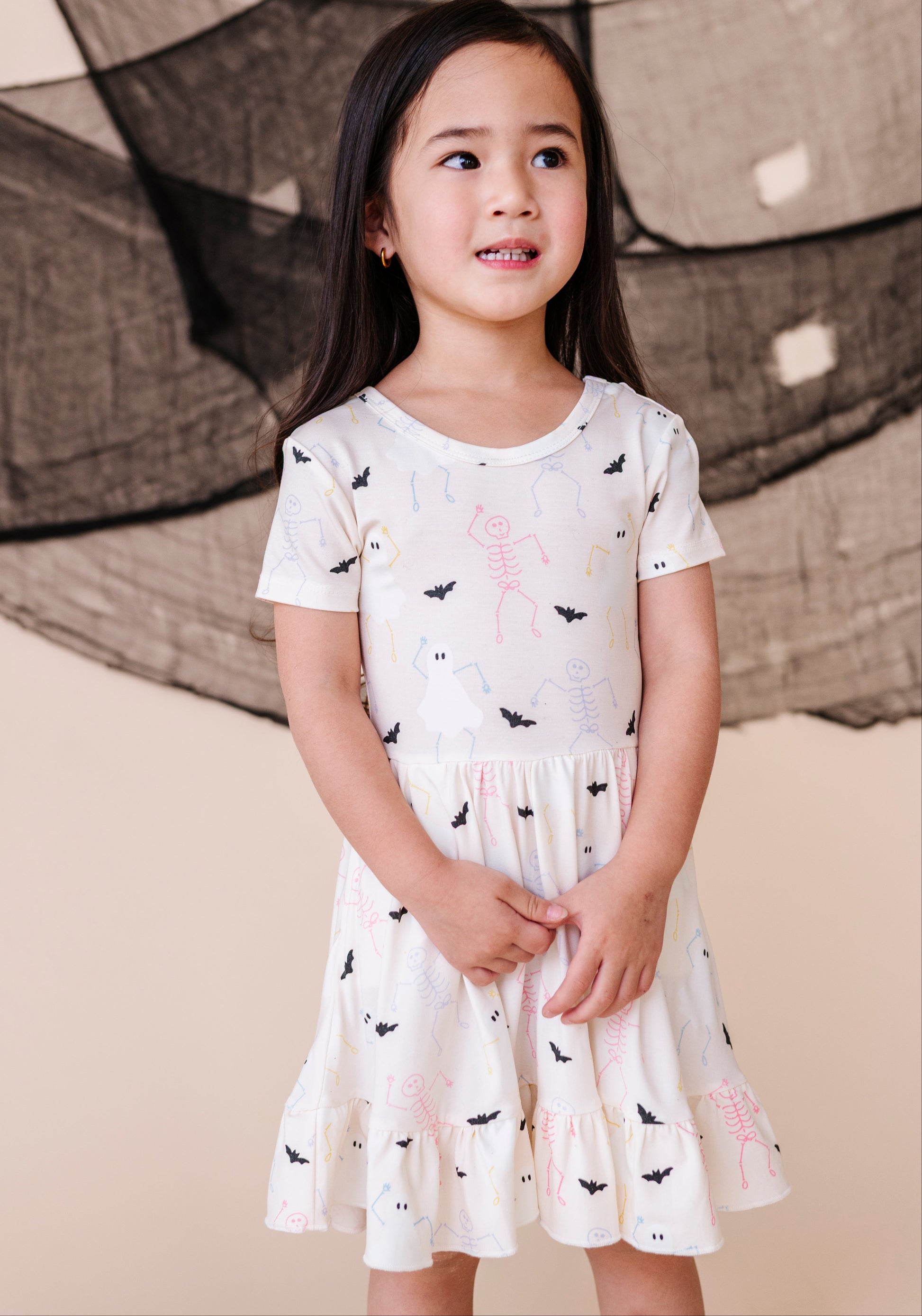 Young girl wearing a white dress with black and pink designs against a neutral background