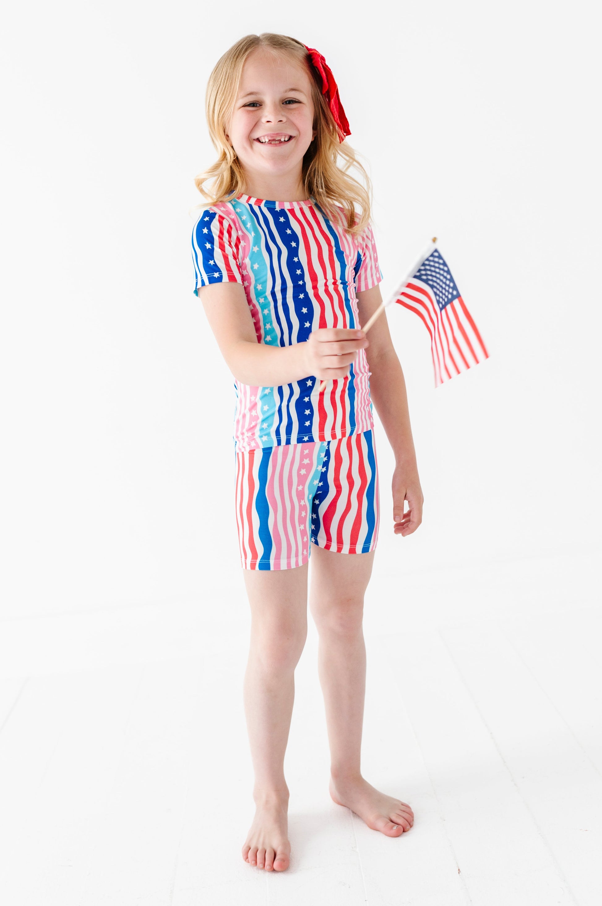 Young girl wearing a colorful striped bamboo pajama set holding an American flag on a white background
