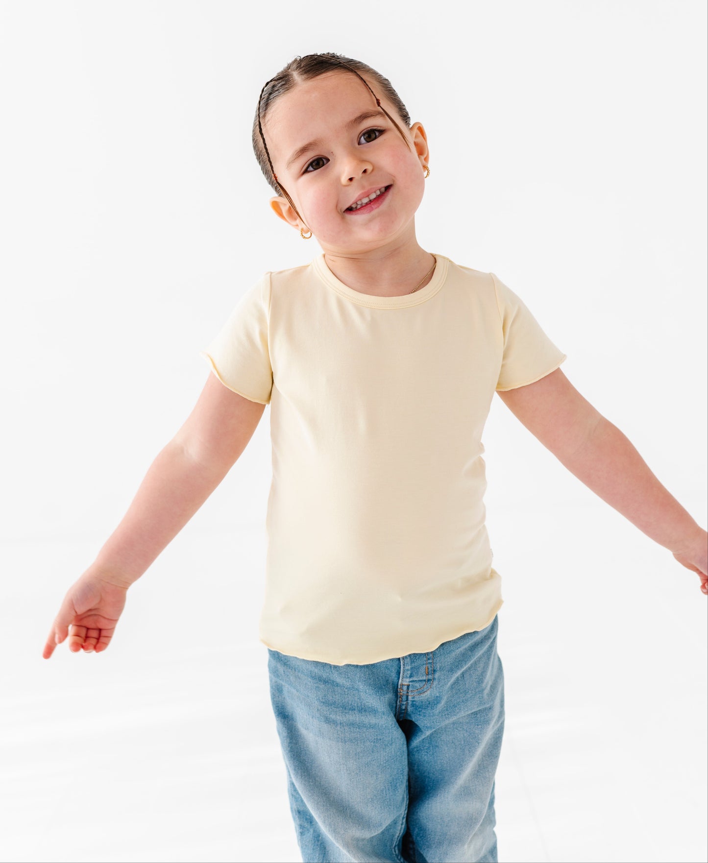 Child wearing a plain yellow t-shirt and blue jeans on a white background