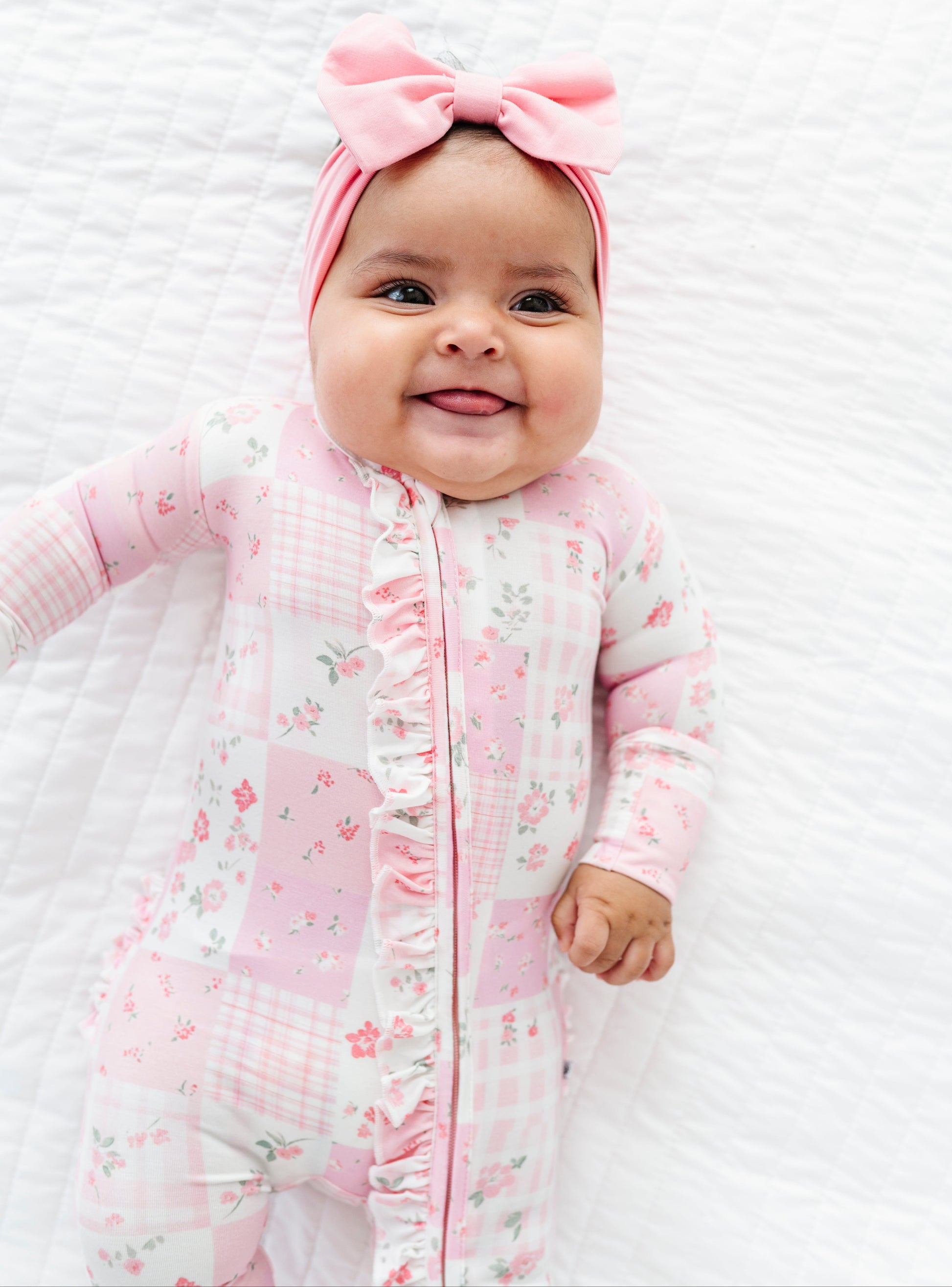 Baby in a pink floral bamboo convertible romper with a matching headband on a white background