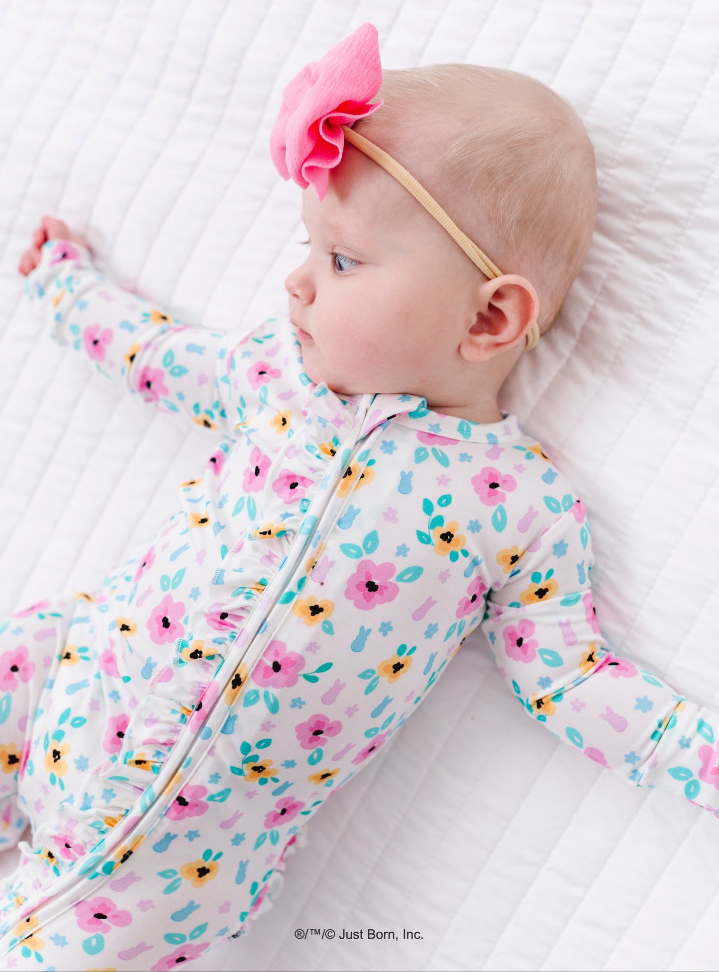 Baby in a floral PEEPS® onesie lying on a white quilted surface