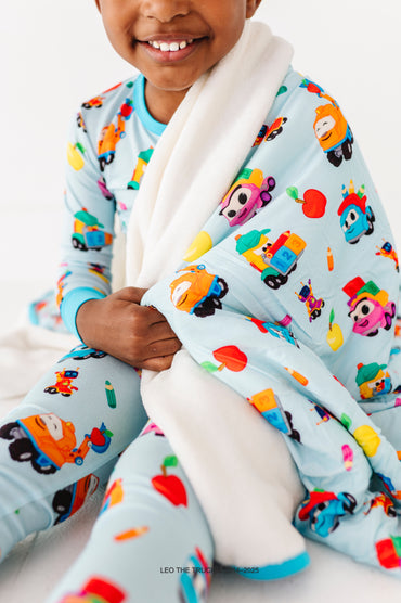 Child wrapped in a colorful bamboo blanket with Leo the Truck design, wearing bamboo pajamas with coordinating prints