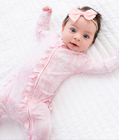 Baby in a pink camo romper with a bow on a white blanket