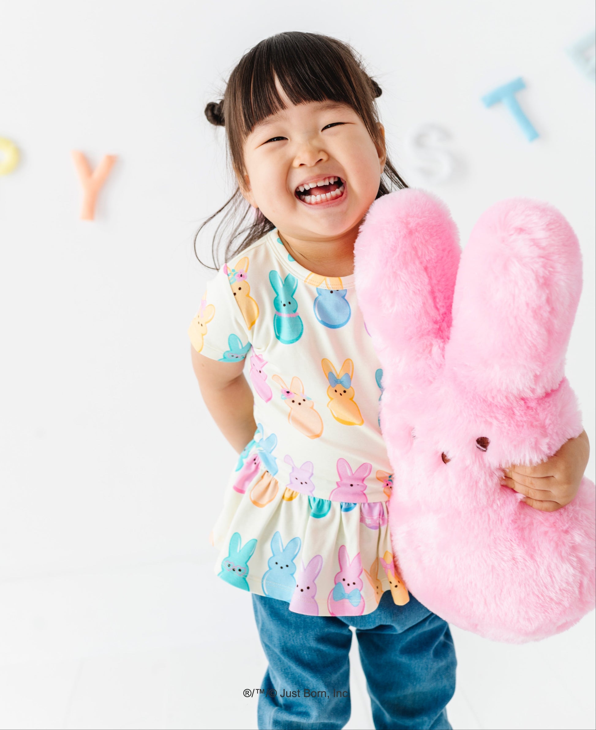 Child holding a pink bunny plush PEEPS®  toy against a white background with colorful letters.