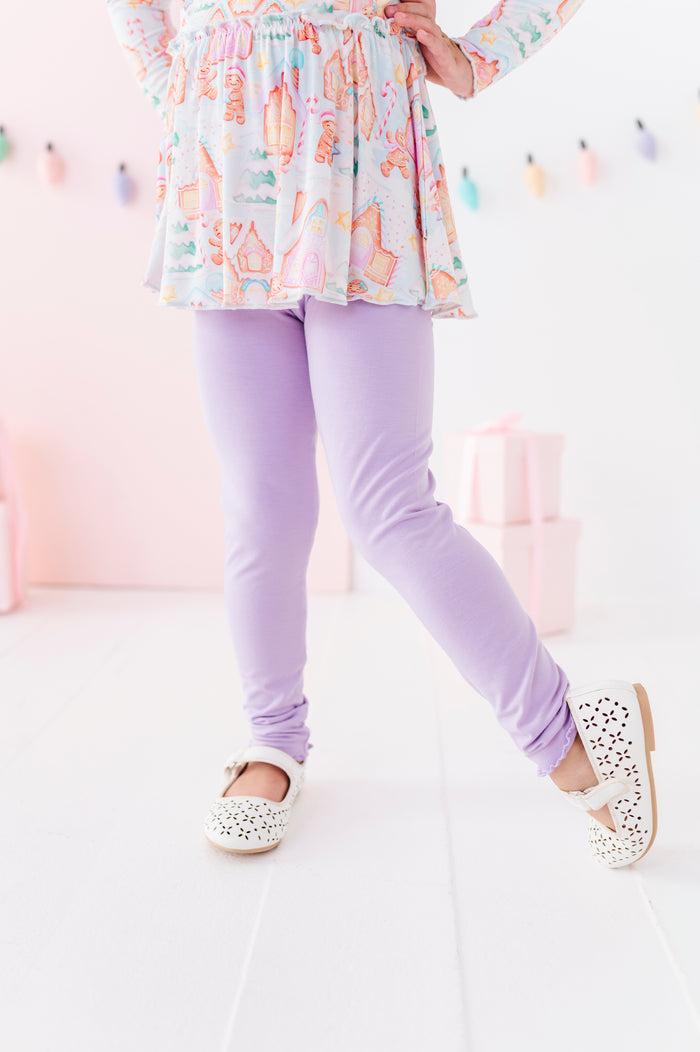 A little girl wearing light purple bamboo leggings standing in a pastel pink Christmas-themed room