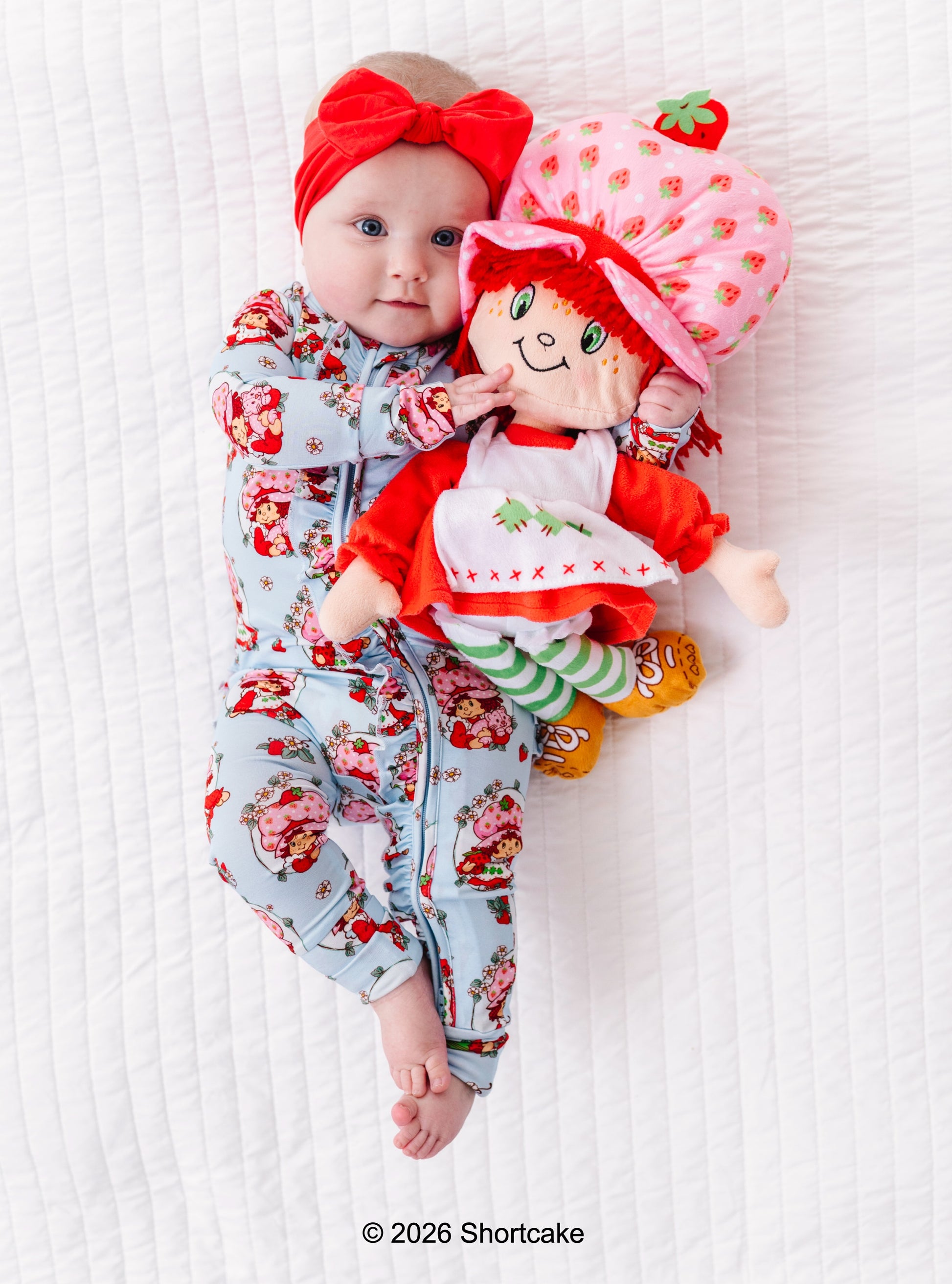 Baby in Strawberry Shortcake™ bamboo pajamas with a matching Strawberry Shortcake™ doll on a white background