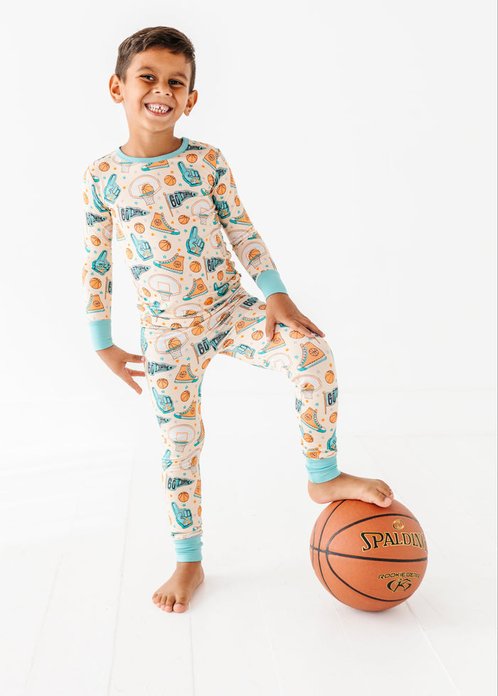 Child wearing a basketball themed bamboo pajama set with his foot perched on a basketball
