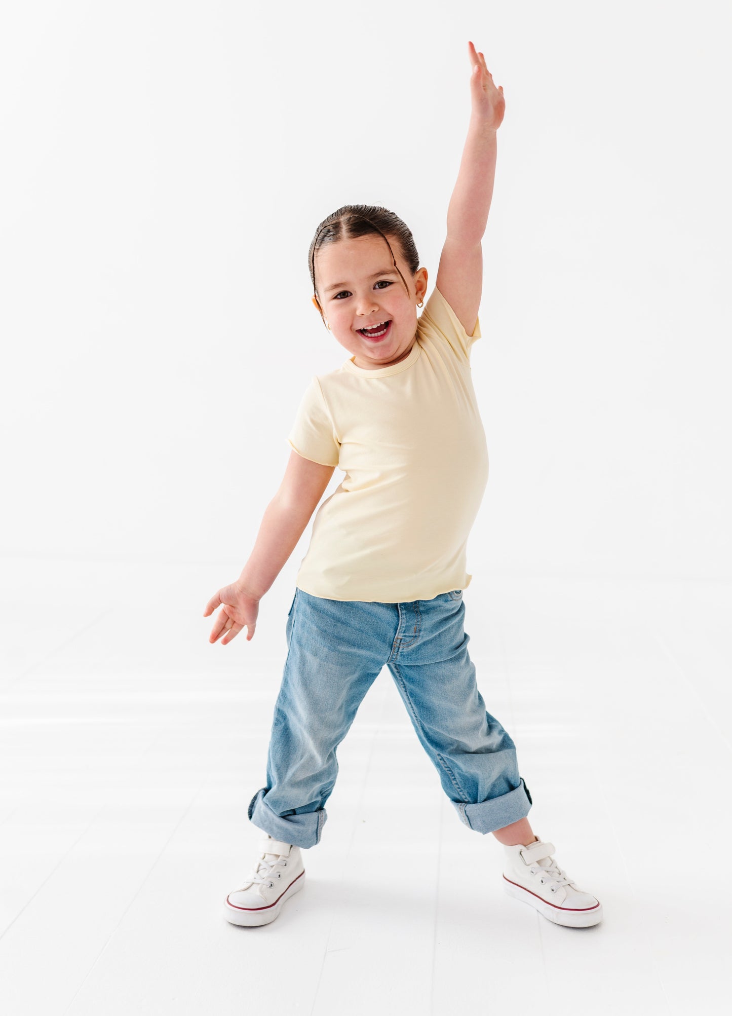 Child wearing a yellow bamboo lettuce-hem shirt and blue jeans on a white background