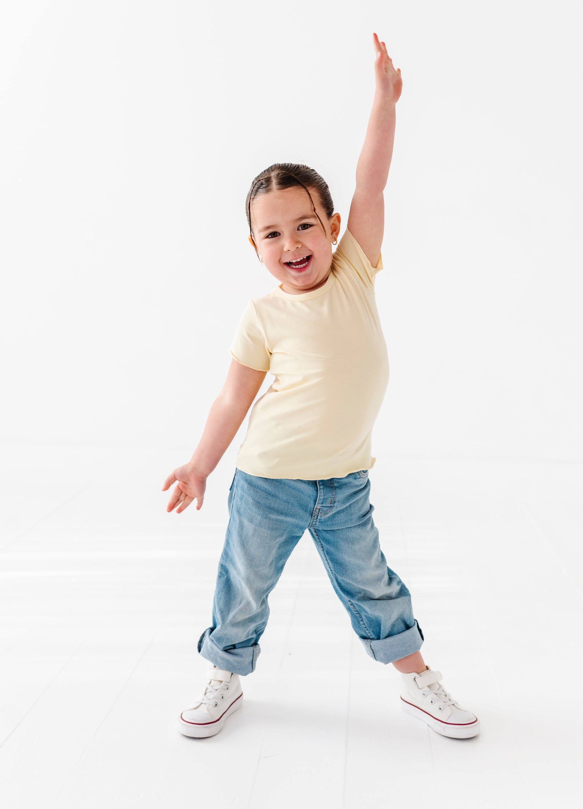 Child wearing a yellow bamboo lettuce-hem shirt and blue jeans on a white background