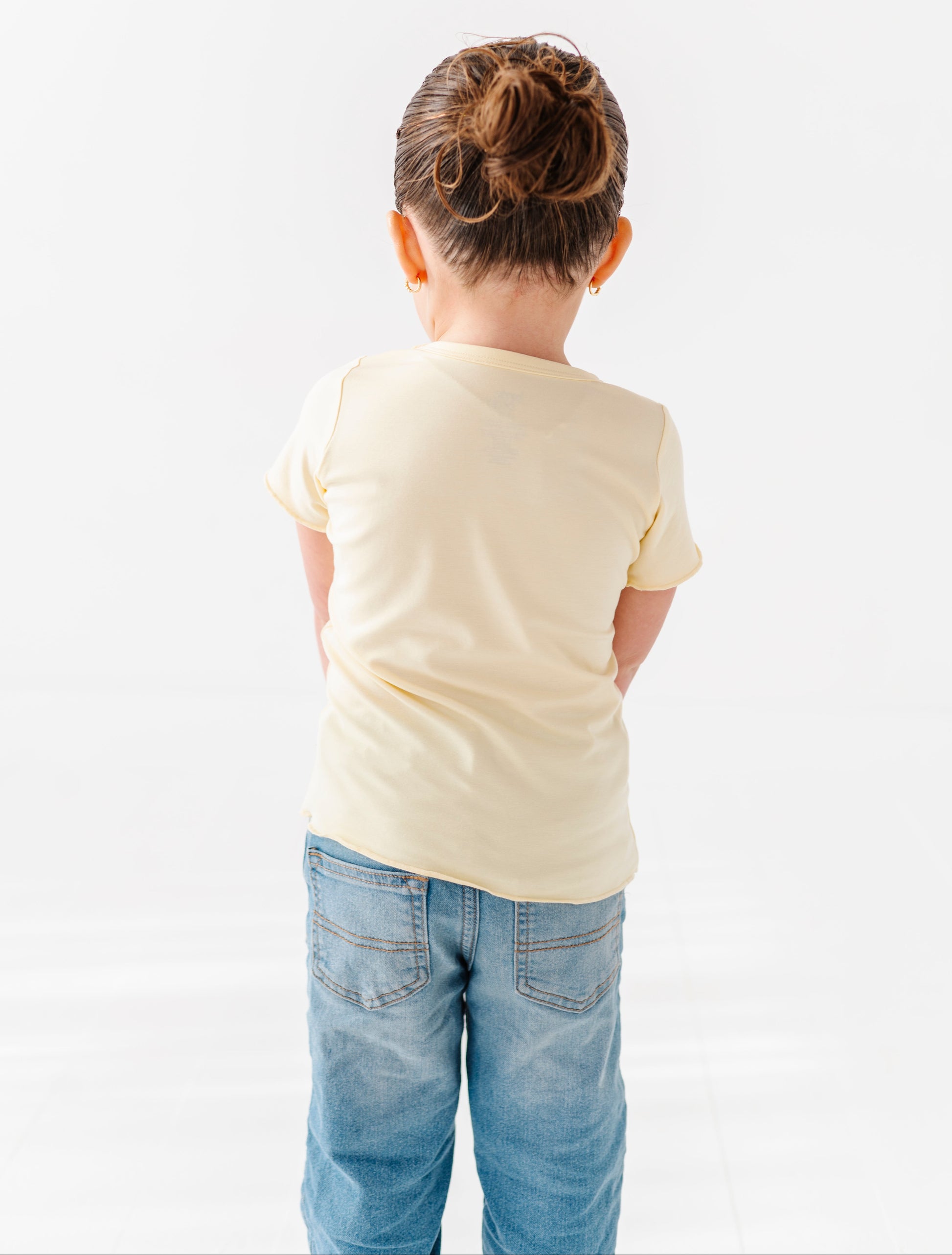 Child wearing a yellow lettuce hem t-shirt and blue jeans on a white background