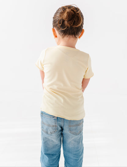 Child wearing a yellow lettuce hem t-shirt and blue jeans on a white background
