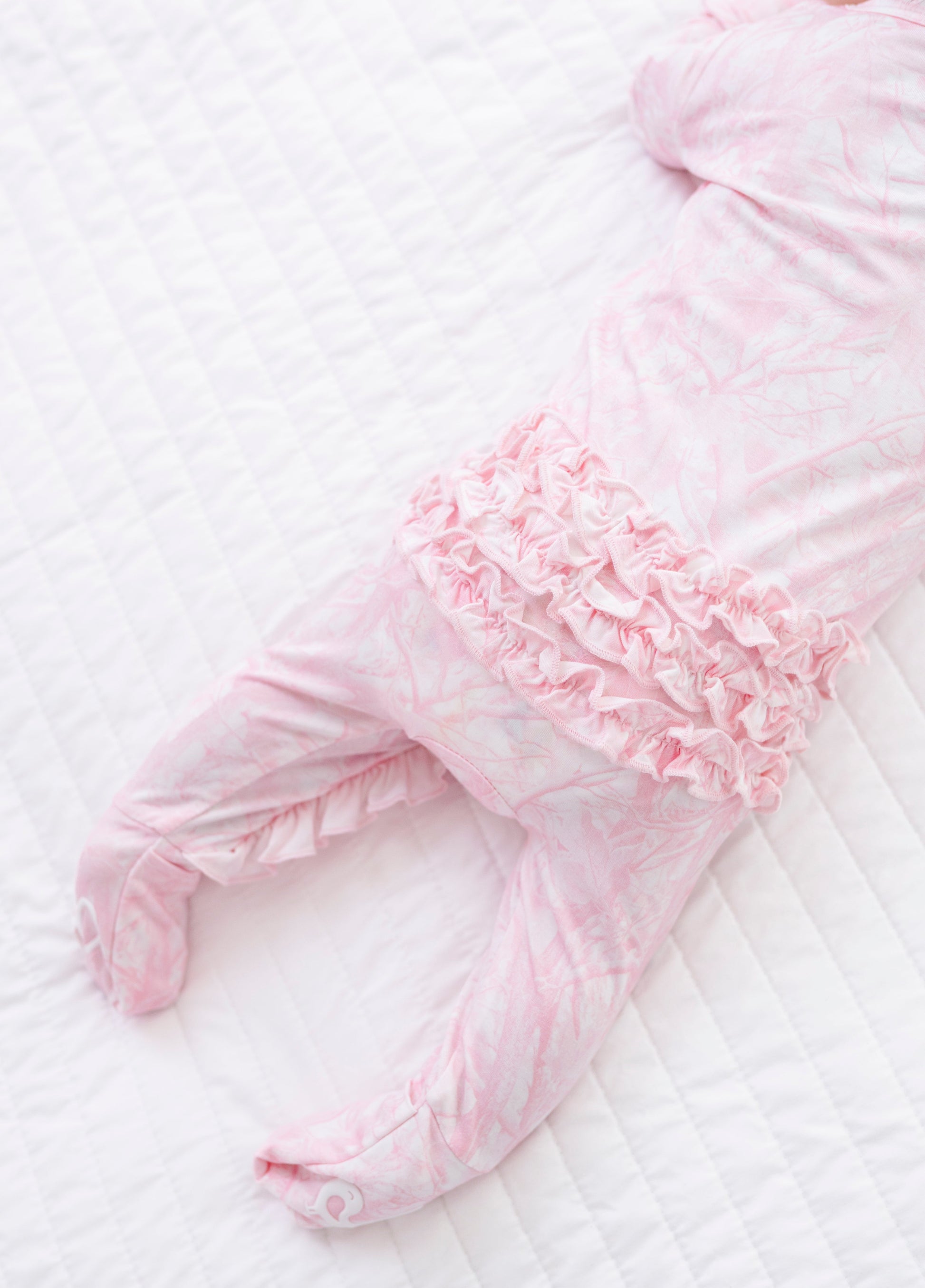 Pink camo baby outfit with ruffles on a white background