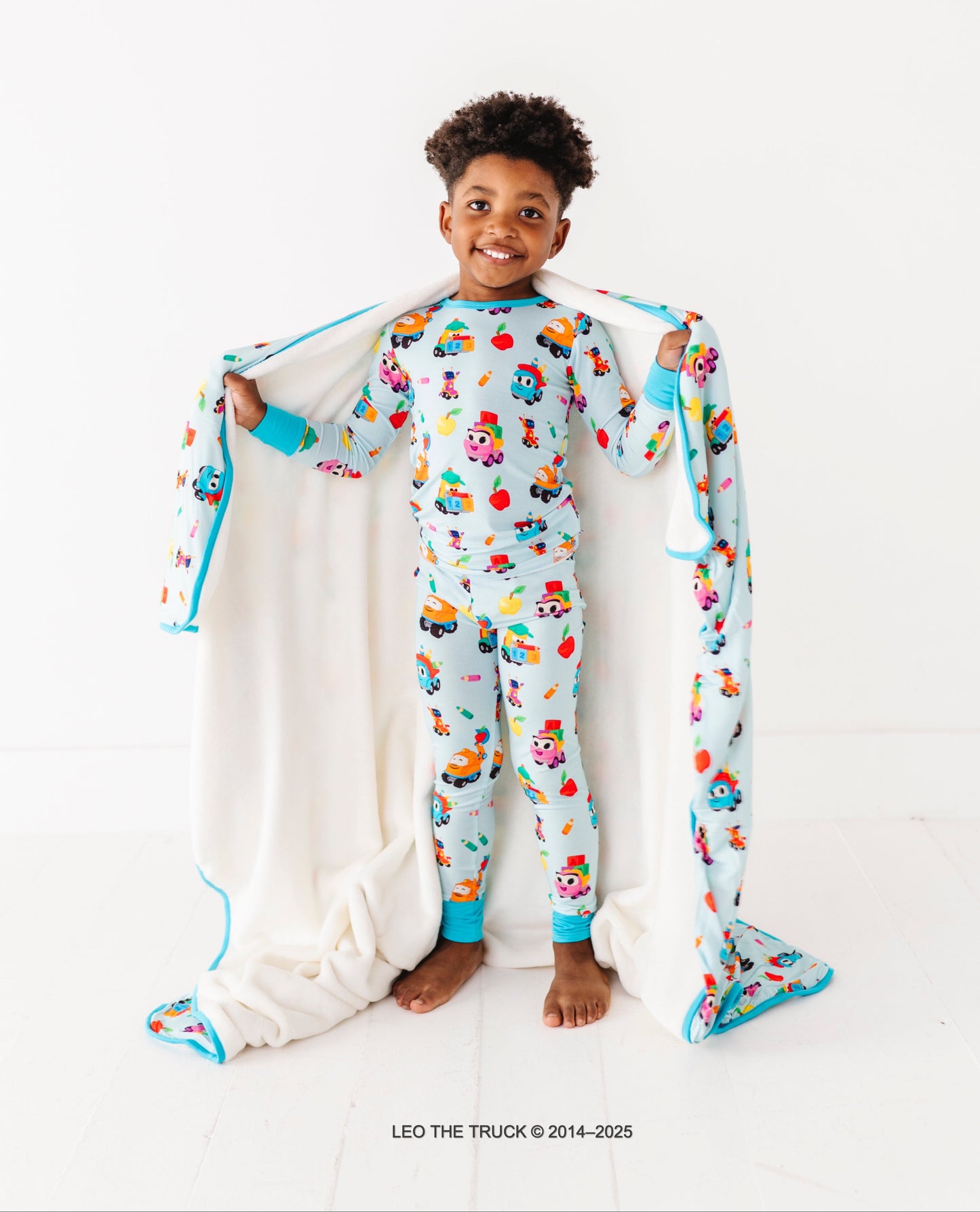 Little boy wearing bamboo Leo the Truck pjs and holding a plush Leo the Truck bamboo blanket 