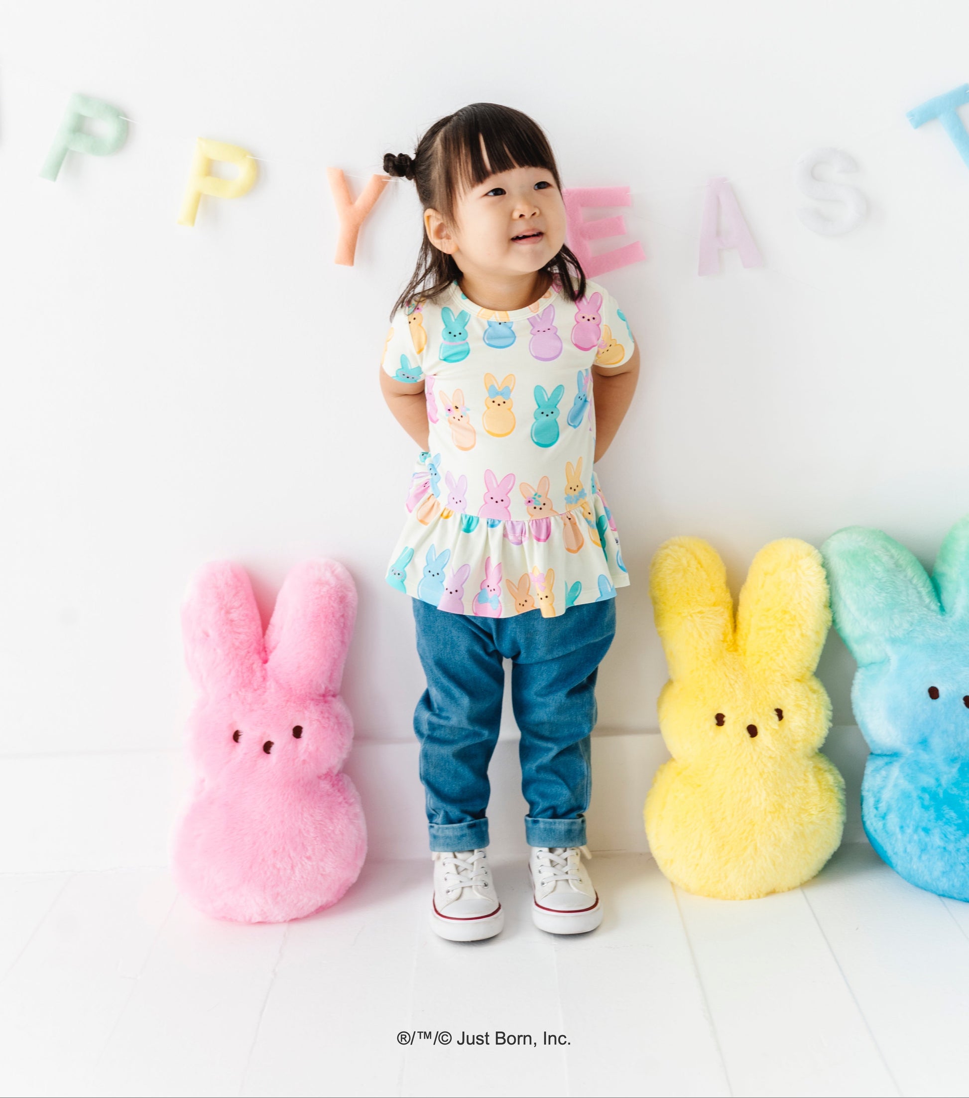 Child wearing a colorful outfit with  PEEPS®  themed clothing, standing next to large plush toys on a white background.