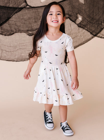 Young girl wearing a cream colored  dress with halloween pattern and black sneakers against a beige background