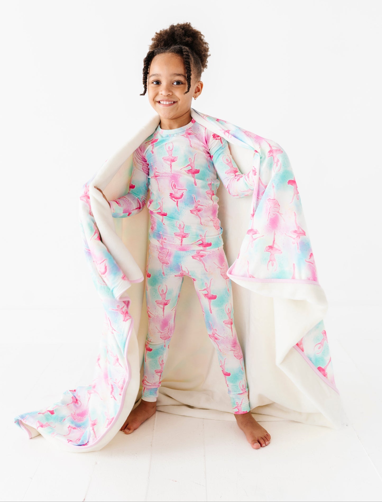 Child wearing a ballet-patterned bamboo pajama set with a matching bamboo plush blanket on a white background
