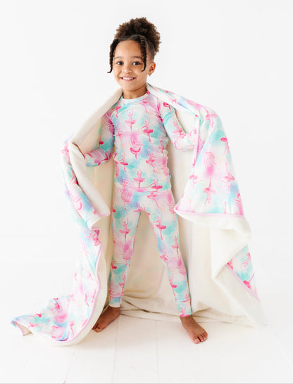 Child wearing a ballet-patterned bamboo pajama set with a matching bamboo plush blanket on a white background