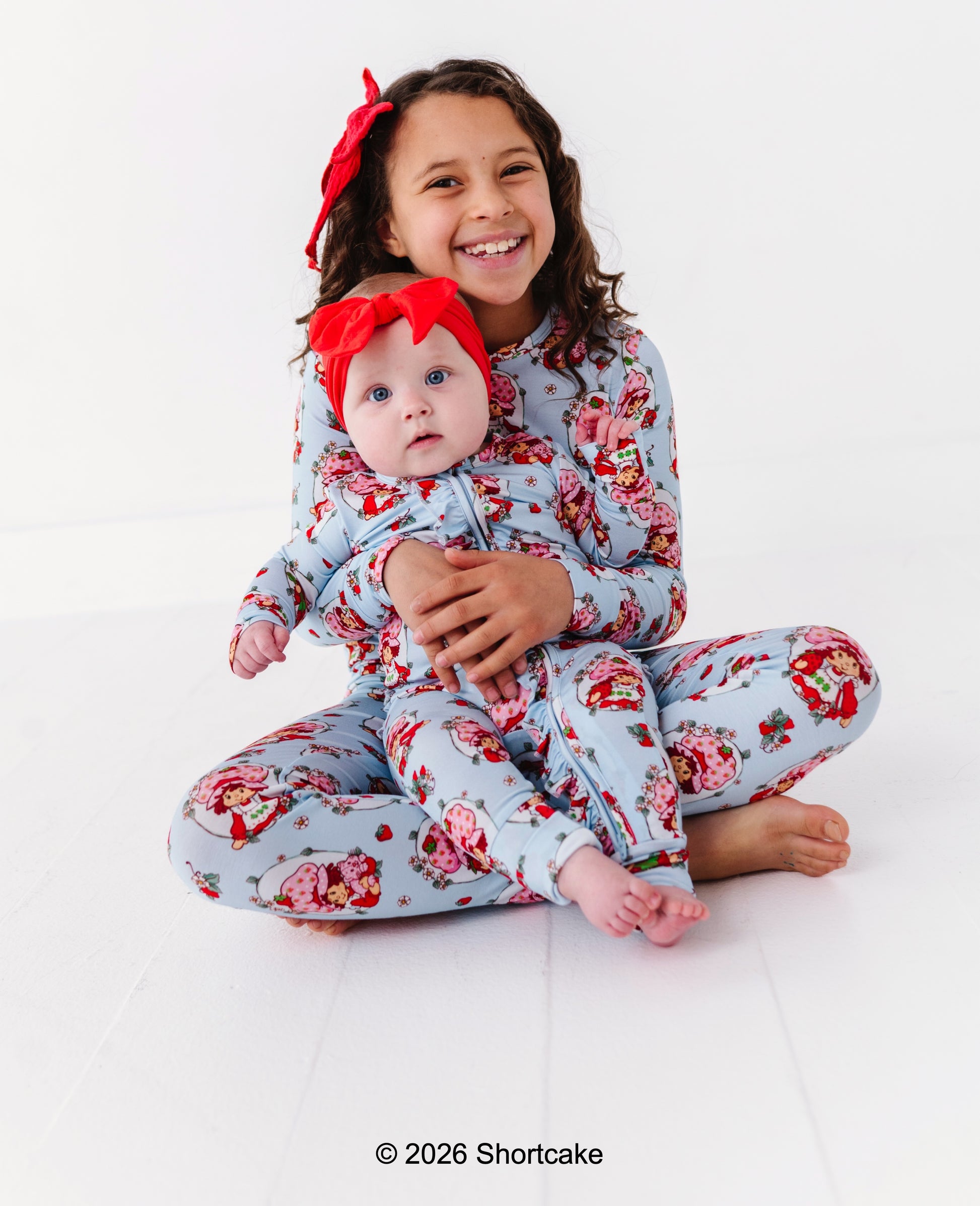 Two children wearing matching Strawberry Shortcake™ pajamas on a white background.