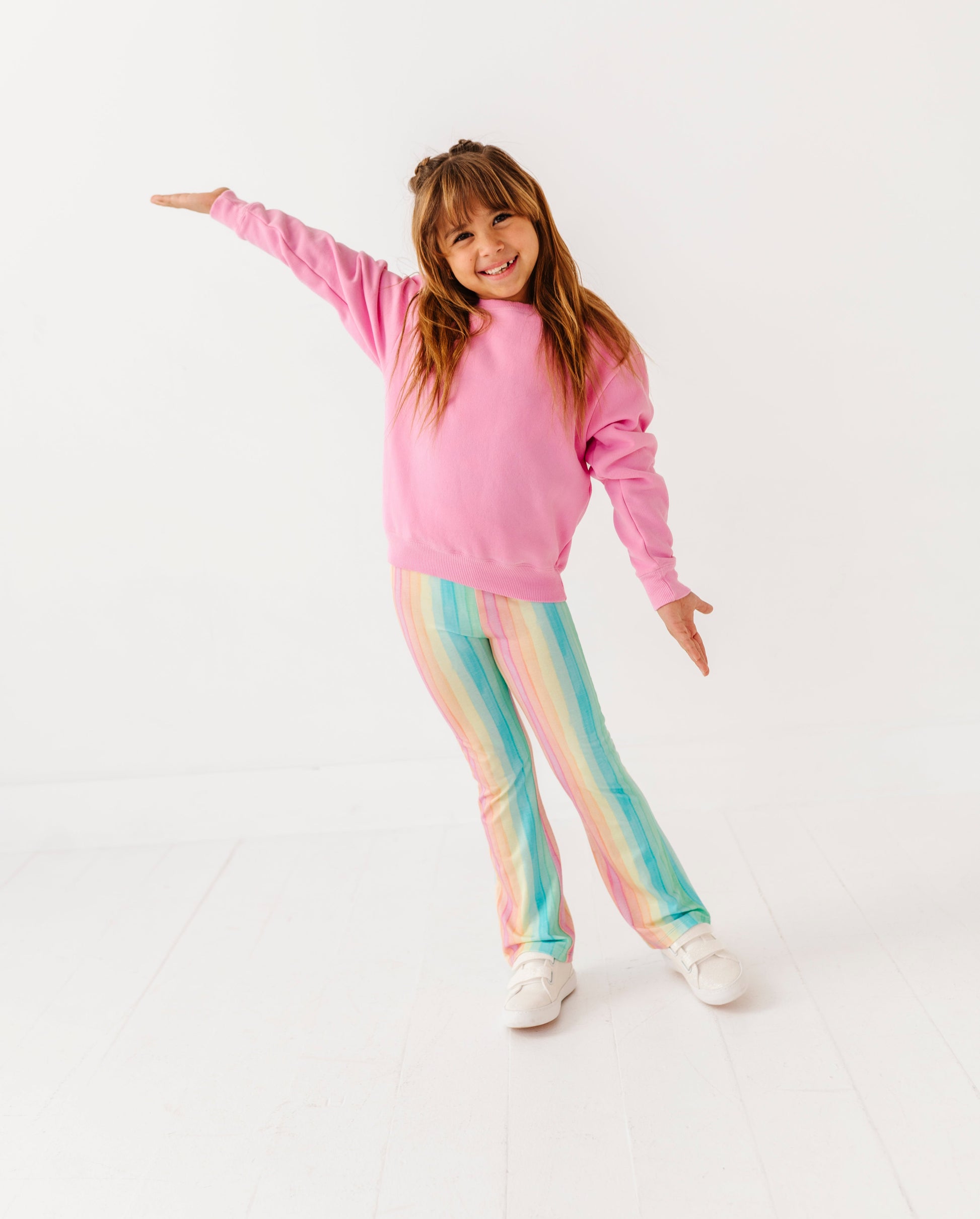 Child wearing a pink sweatshirt and colorful pants on a white background