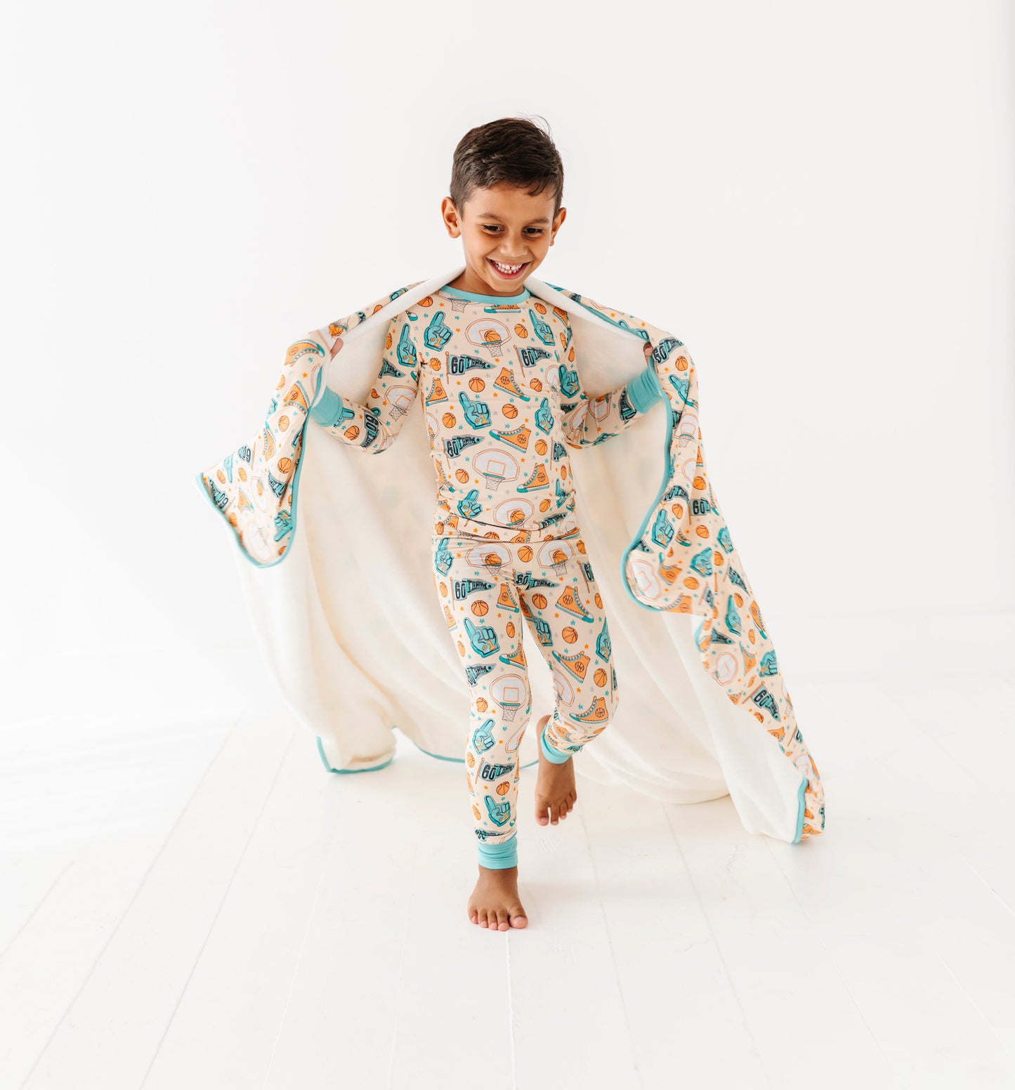 Child wearing a basketball-themed bamboo pajama set with a matching bamboo blanket on a white background