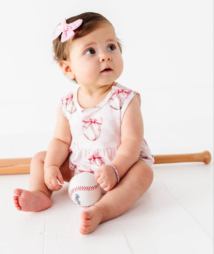 Baby girl sitting on a white surface holding a baseball and bat