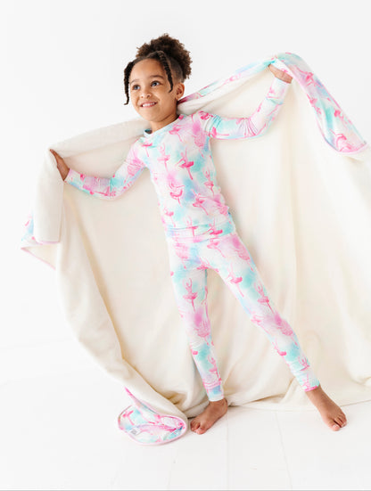 Child wearing a colorful ballet-themed bamboo pajamas, sitting on a white surface with a bamboo plush blanket.