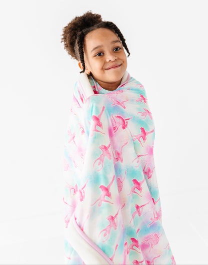 Child wearing a colorful ballet-patterned bamboo plush blanket against a white background