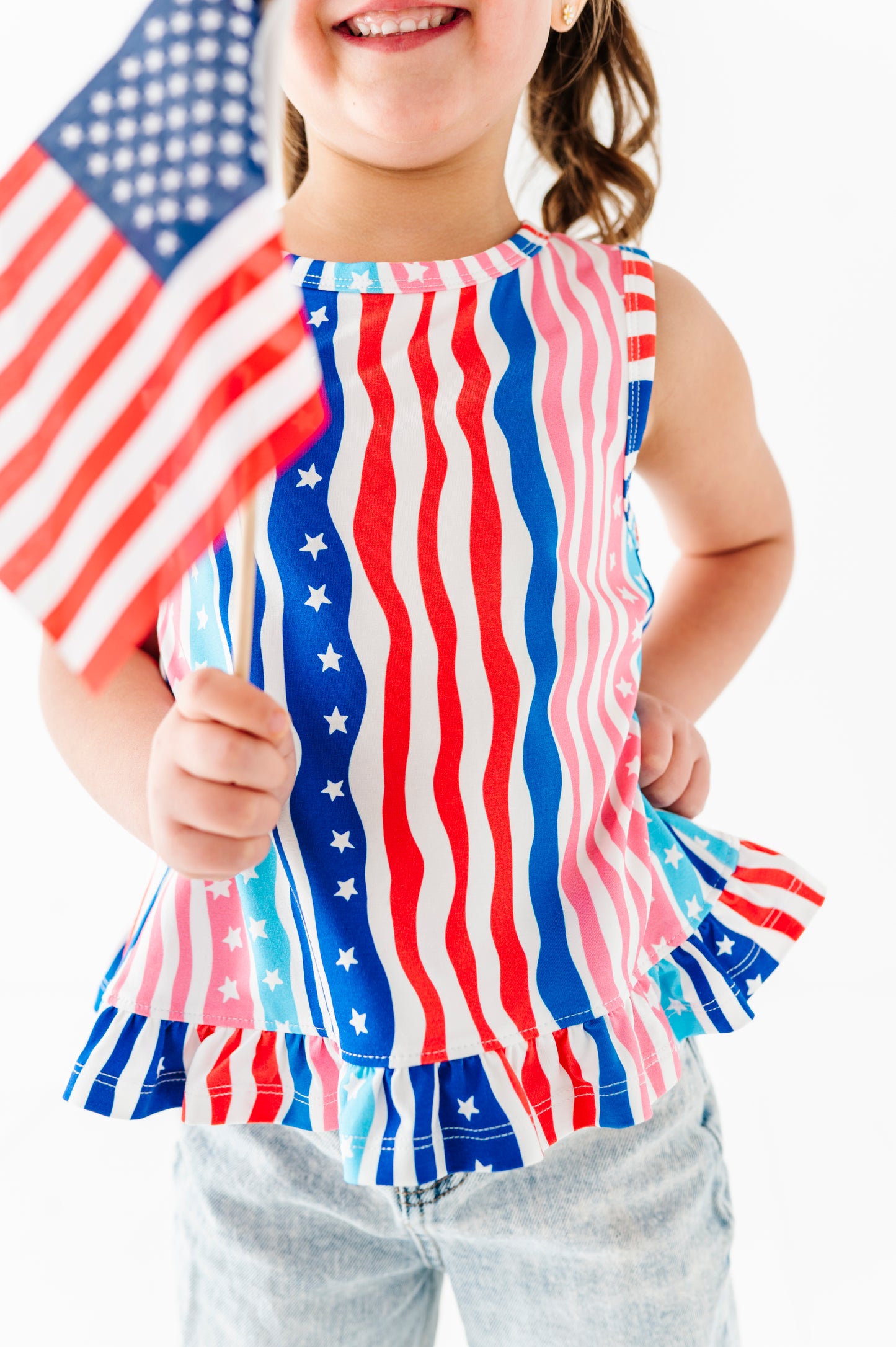 Child wearing a red, white, and blue striped top with an American flag pattern, holding a small American flag.