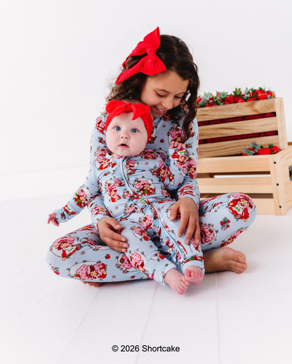 Two children in matching Strawberry Shortcake™ bamboo pajamas with red bows sitting on a white surface.
