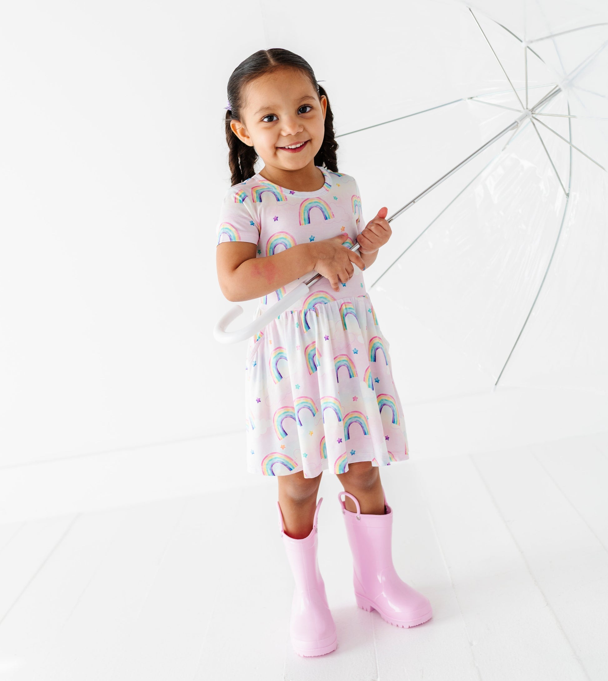 Young girl in a rainbow bamboo dress and pink boots holding an umbrella on a white background