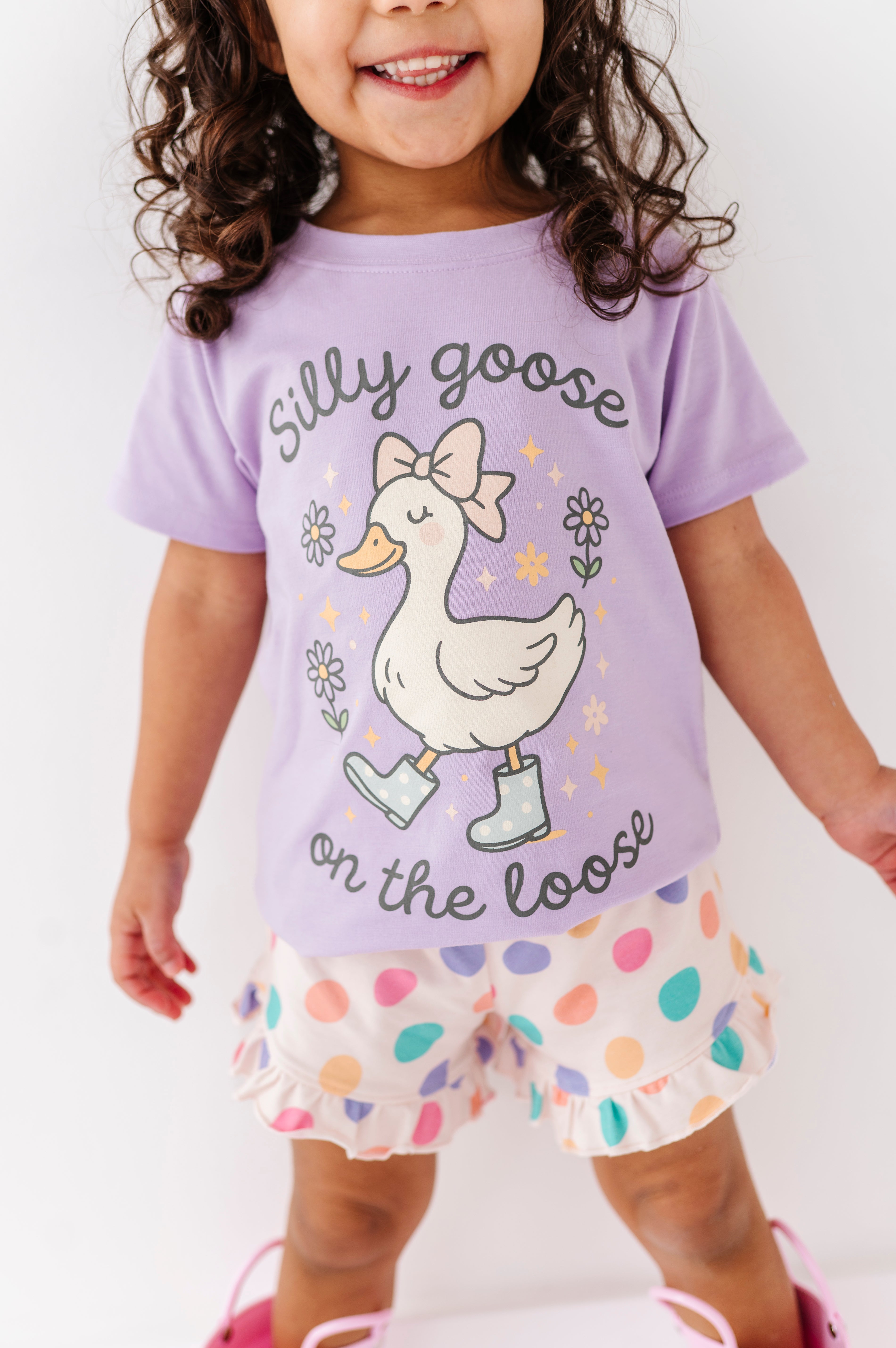 Child wearing a purple shirt with a goose graphic and shorts with colorful patterns on a white background