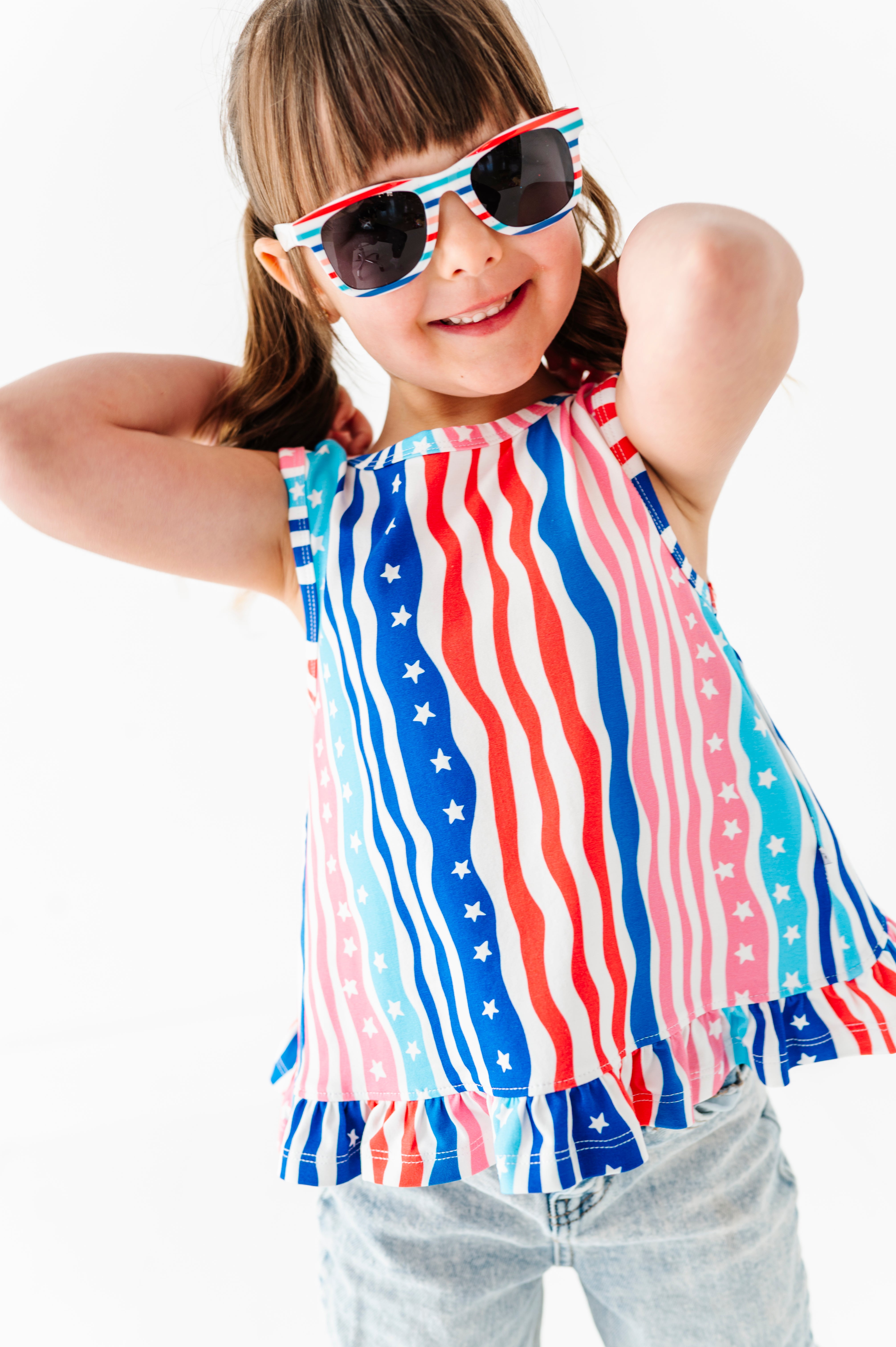 Child wearing a colorful American flag top and sunglasses on a white background