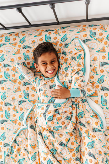 Child wearing sports themed bamboo pajamas, wrapped in a basketball themed blanket, lying on a sports focused bamboo sheet