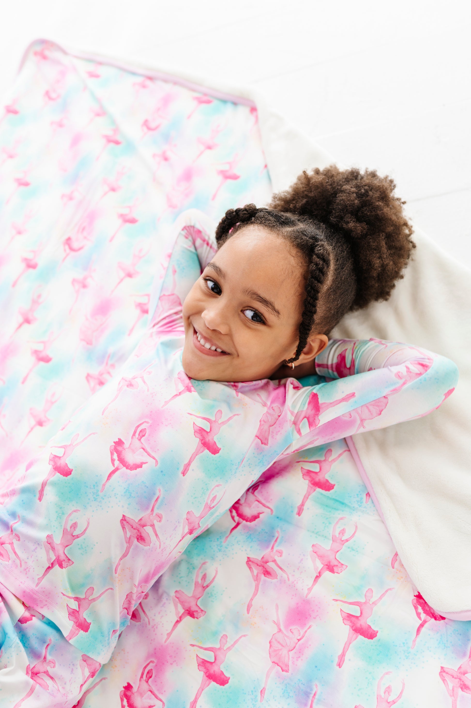 Child lying under a colorful quilt with ballet pattern on a white background