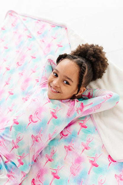 Child lying under a colorful quilt with ballet pattern on a white background