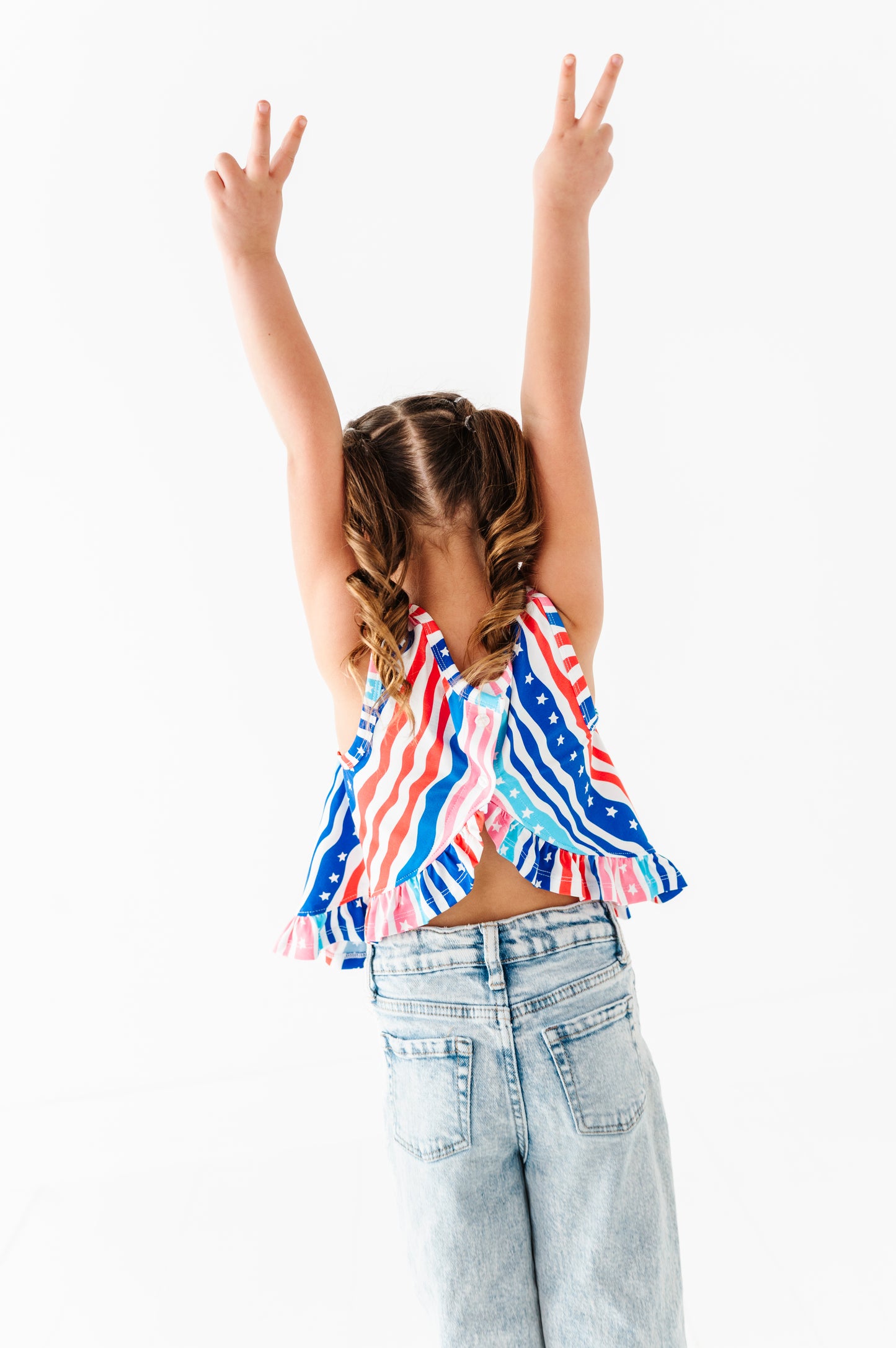 Young girl wearing a colorful striped bamboo-cotton top and light blue jeans with arms raised on a white background