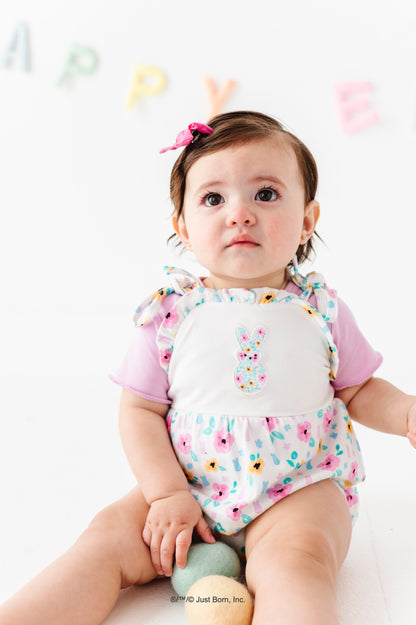 Baby wearing a colorful PEEPS® romper, sitting on a white surface.