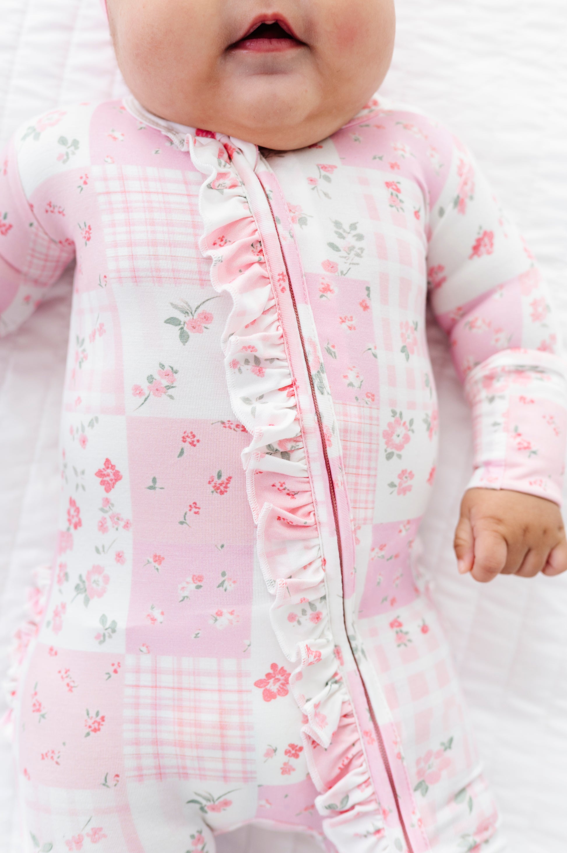 Baby in a pink floral and checkered bamboo zip romper outfit with ruffled details.