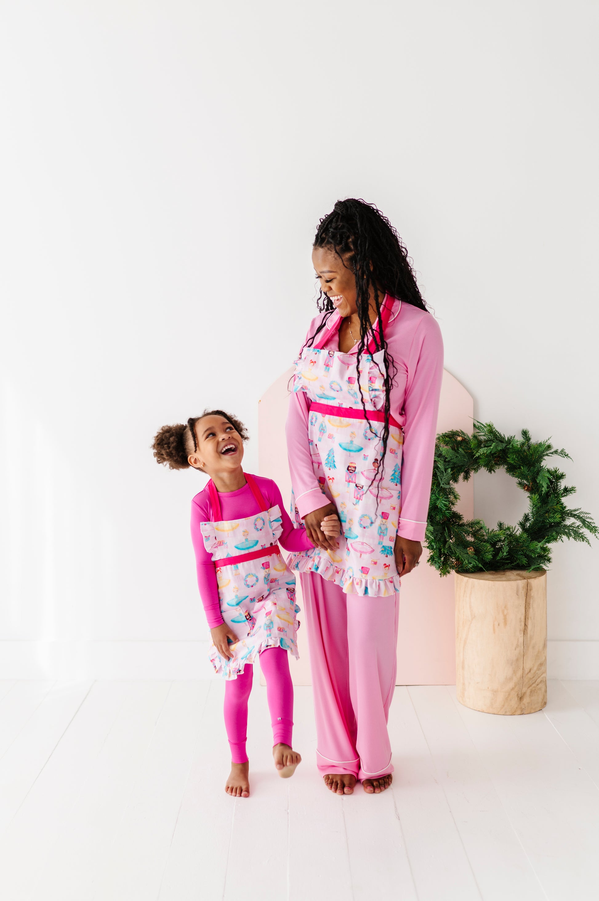 Matching mom and child Sugarplum holiday baking aprons with a wreath in the background 