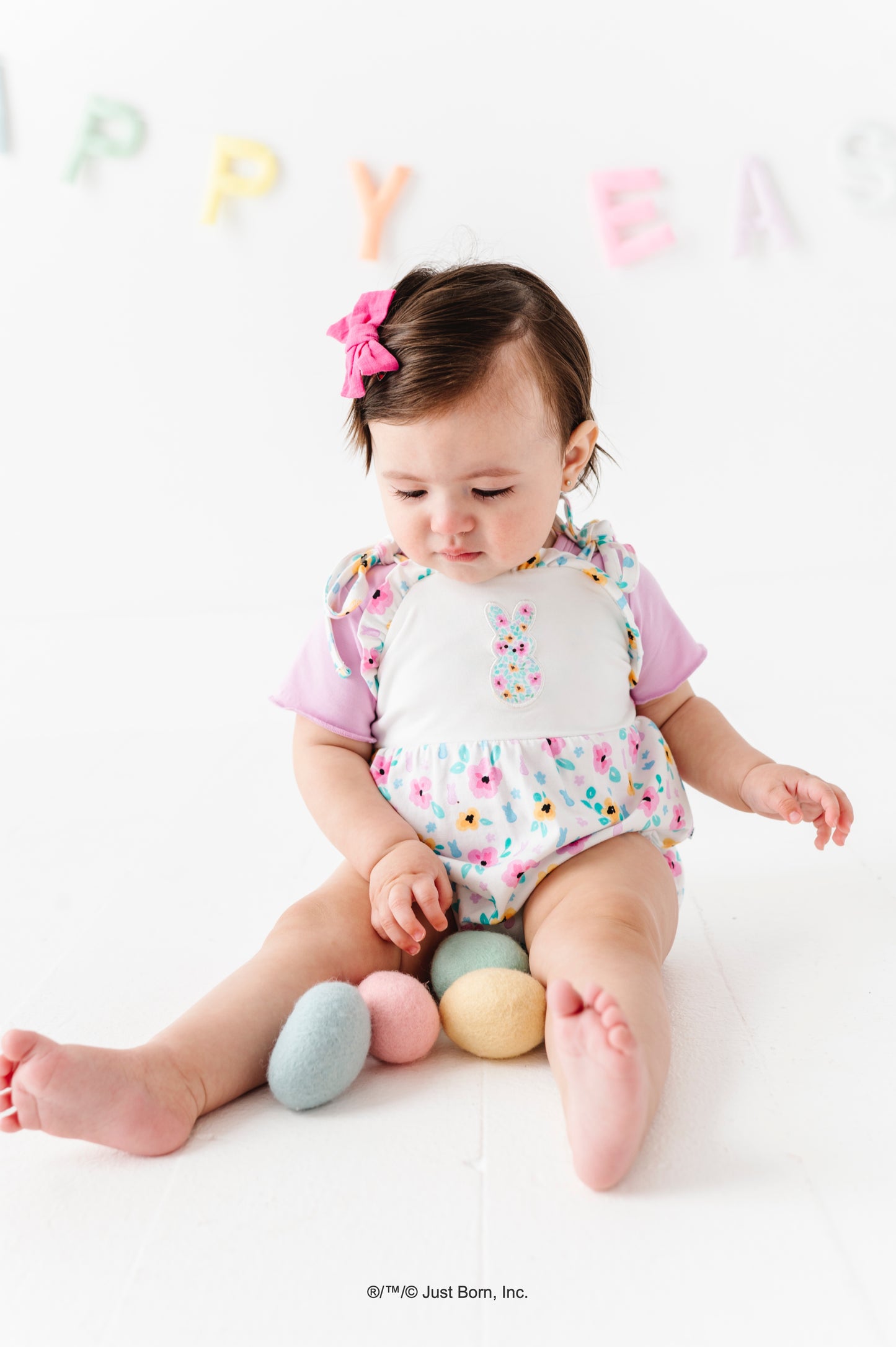Baby sitting on a white surface with colorful eggs and 'Happy Easter' letters in the background