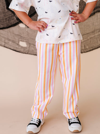 Child wearing a white top with halloween patterns and striped pants on a beige background