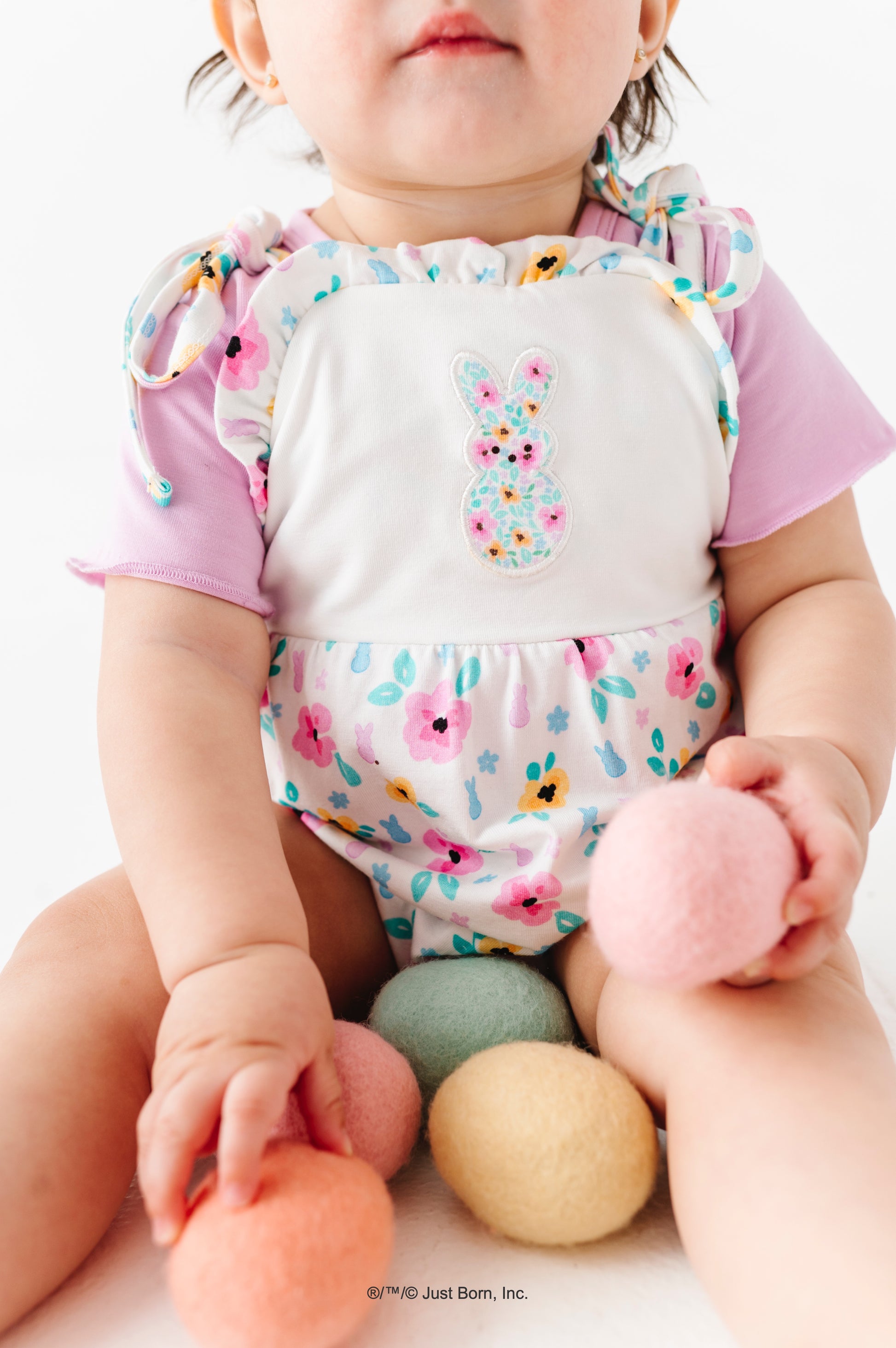 Baby wearing a colorful PEEPS® outfit and floral romper with pastel-colored eggs.