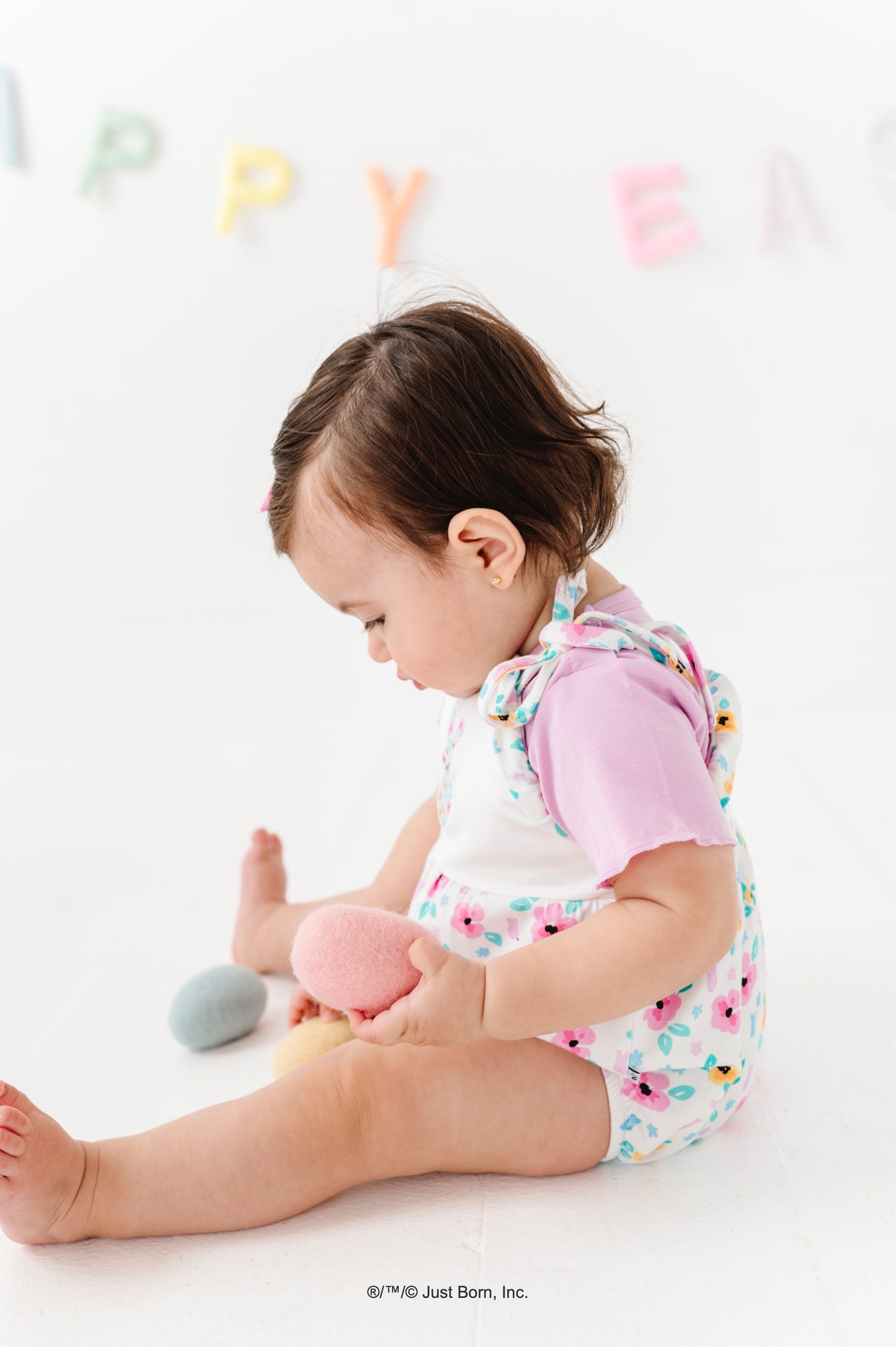Baby wearing a PEEPS® bamboo romper playing with toys on a white floor with colorful letters in the background