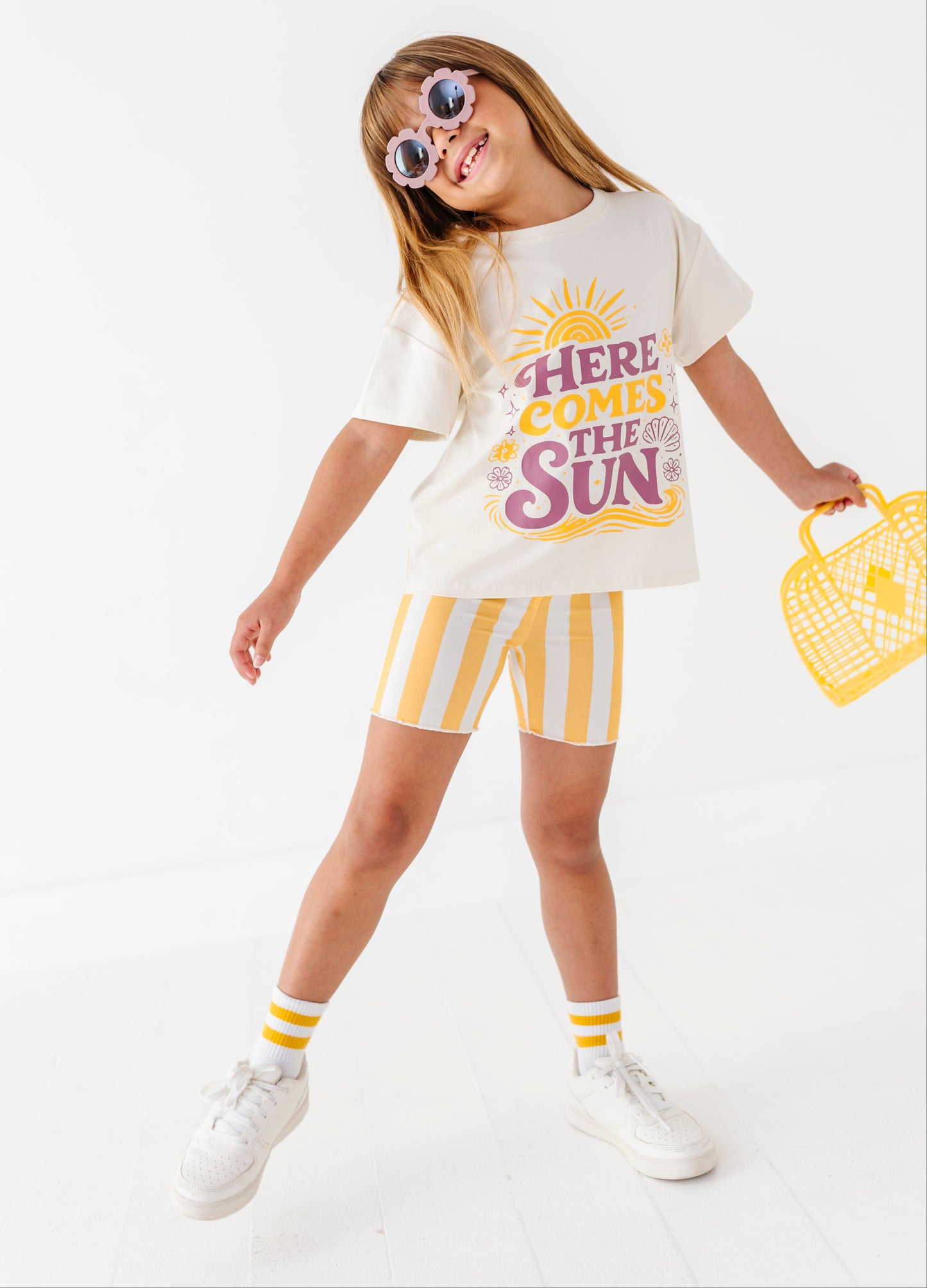 Child wearing a 'Here Comes the Sun' t-shirt and yellow striped shorts on a white background