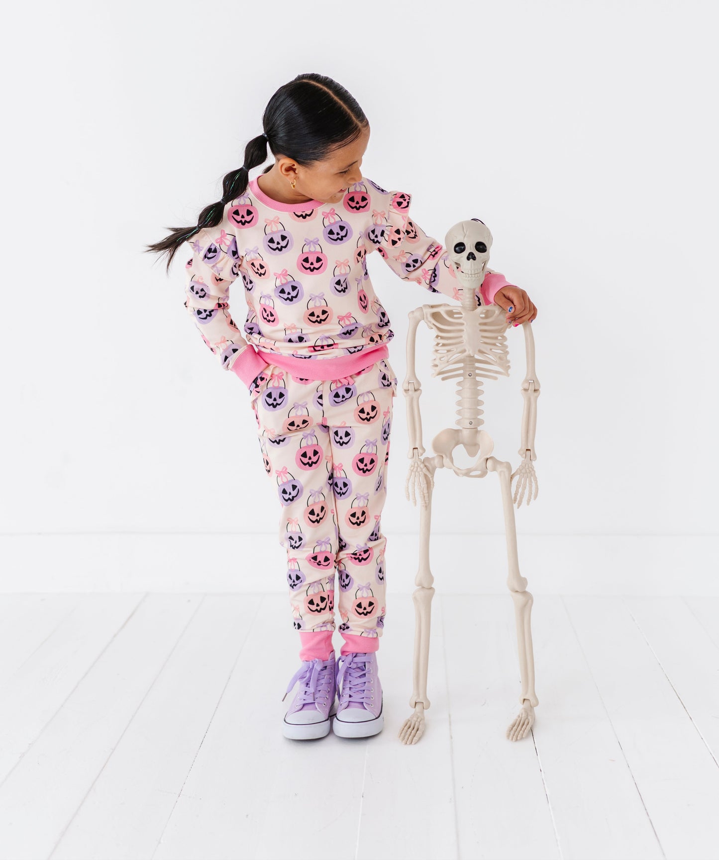 Child wearing a Halloween-themed bamboo pajama set with a skeleton on a white floor.