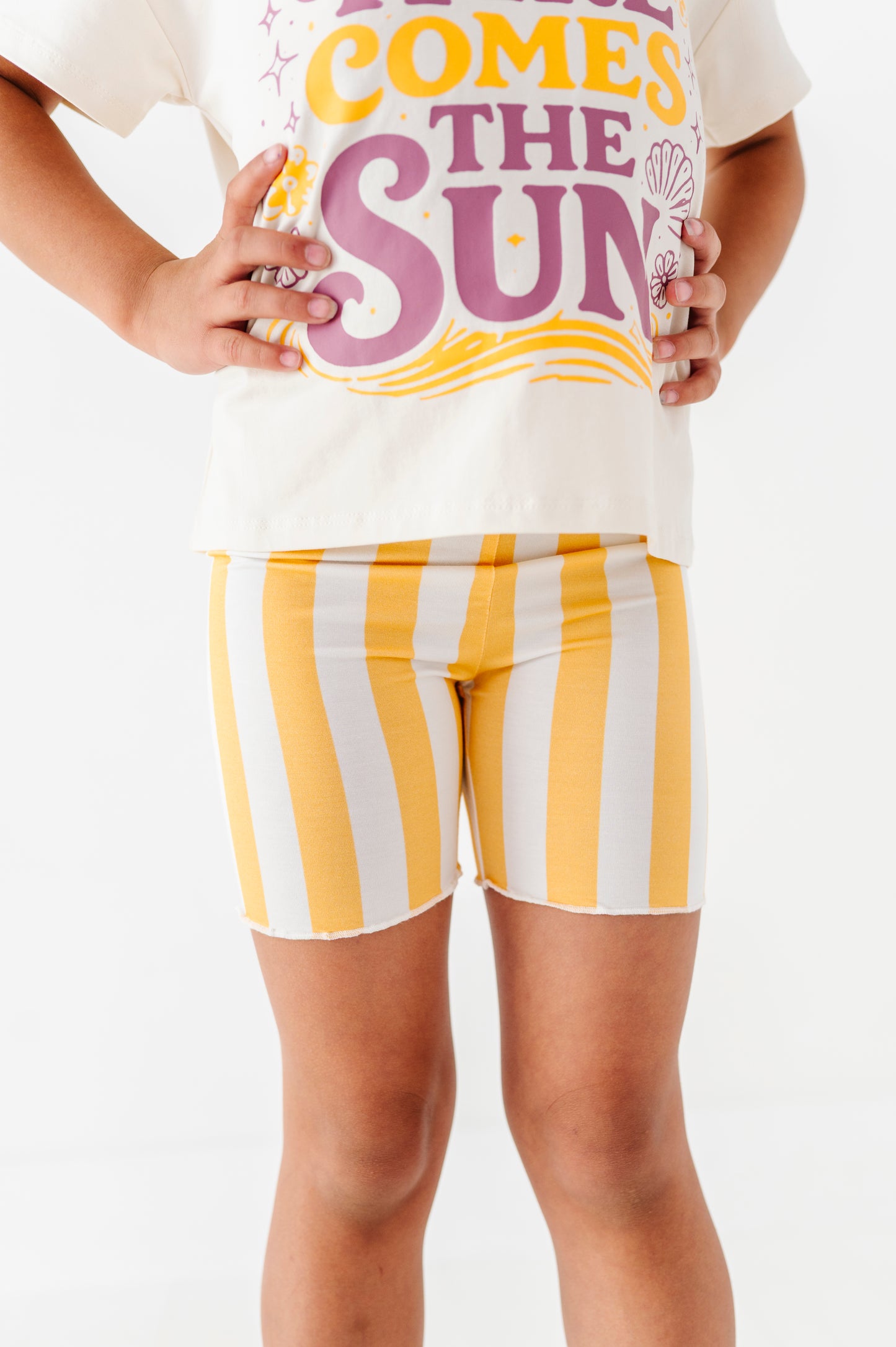 Girl wearing a white t-shirt with colorful text and yellow and white striped shorts on a white background