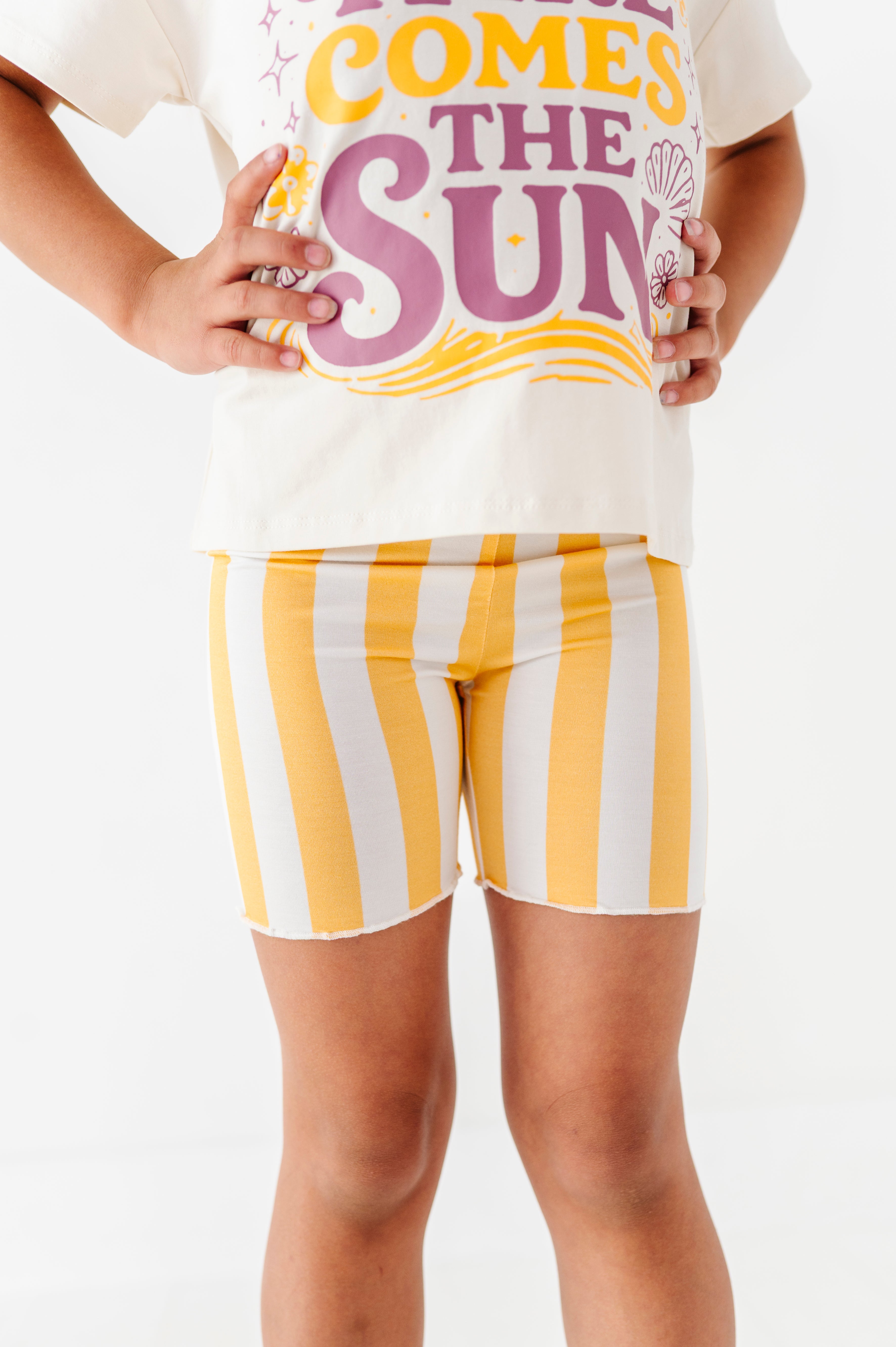 Girl wearing a white t-shirt with colorful text and yellow and white striped shorts on a white background