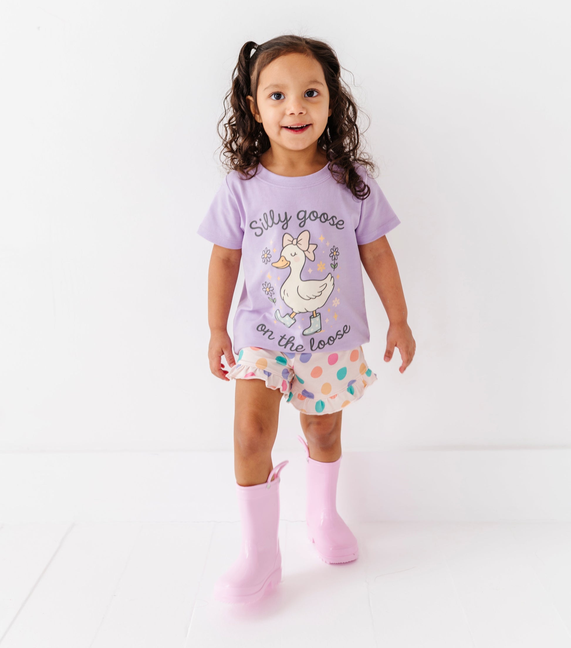 Young girl wearing a purple t-shirt with a goose design and patterned shorts on a white background
