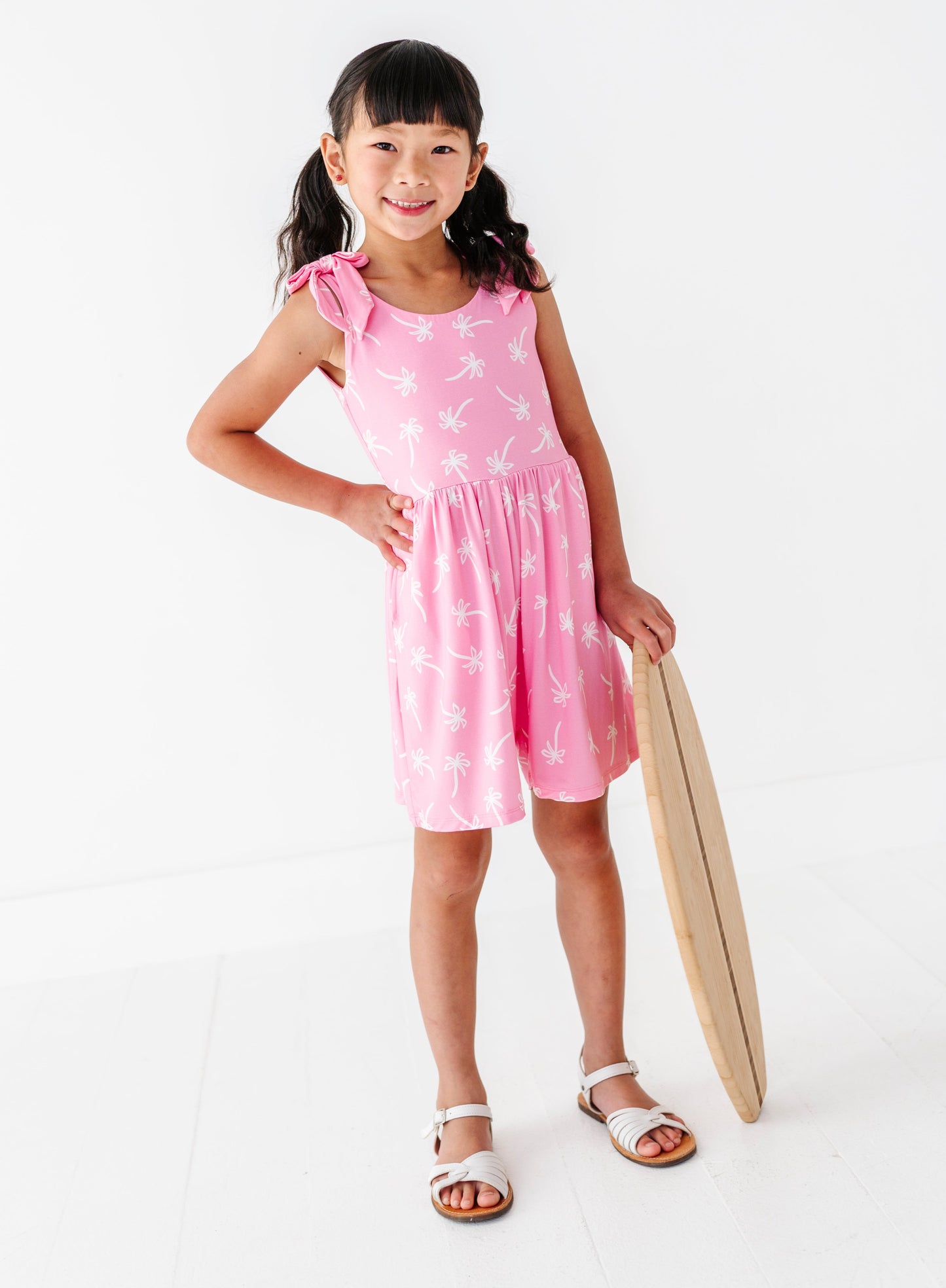 Young girl in a pink dress with white patterns, holding a wooden paddle, on a white background