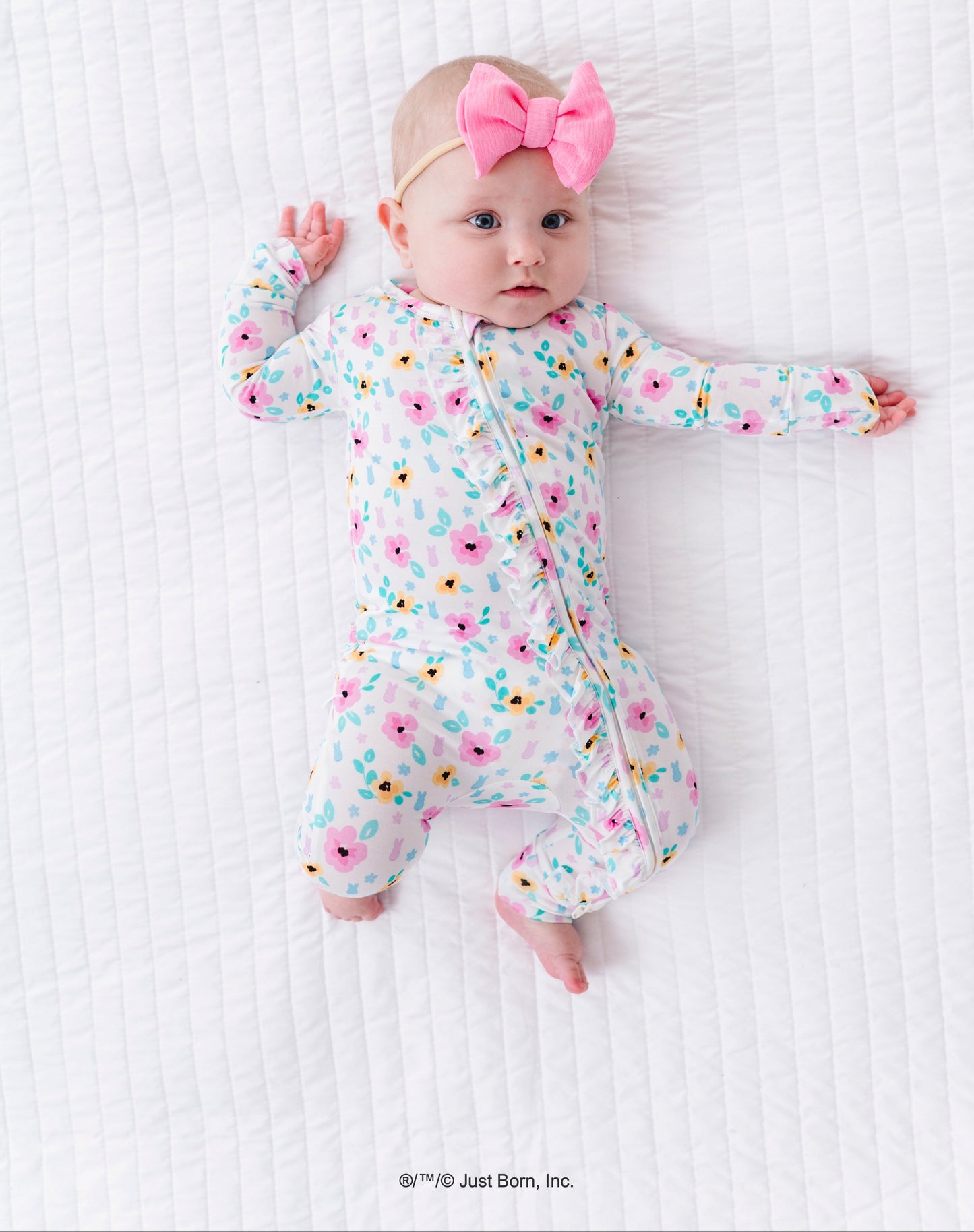 Baby in a floral PEEPS® romper with a pink bow on a white textured surface